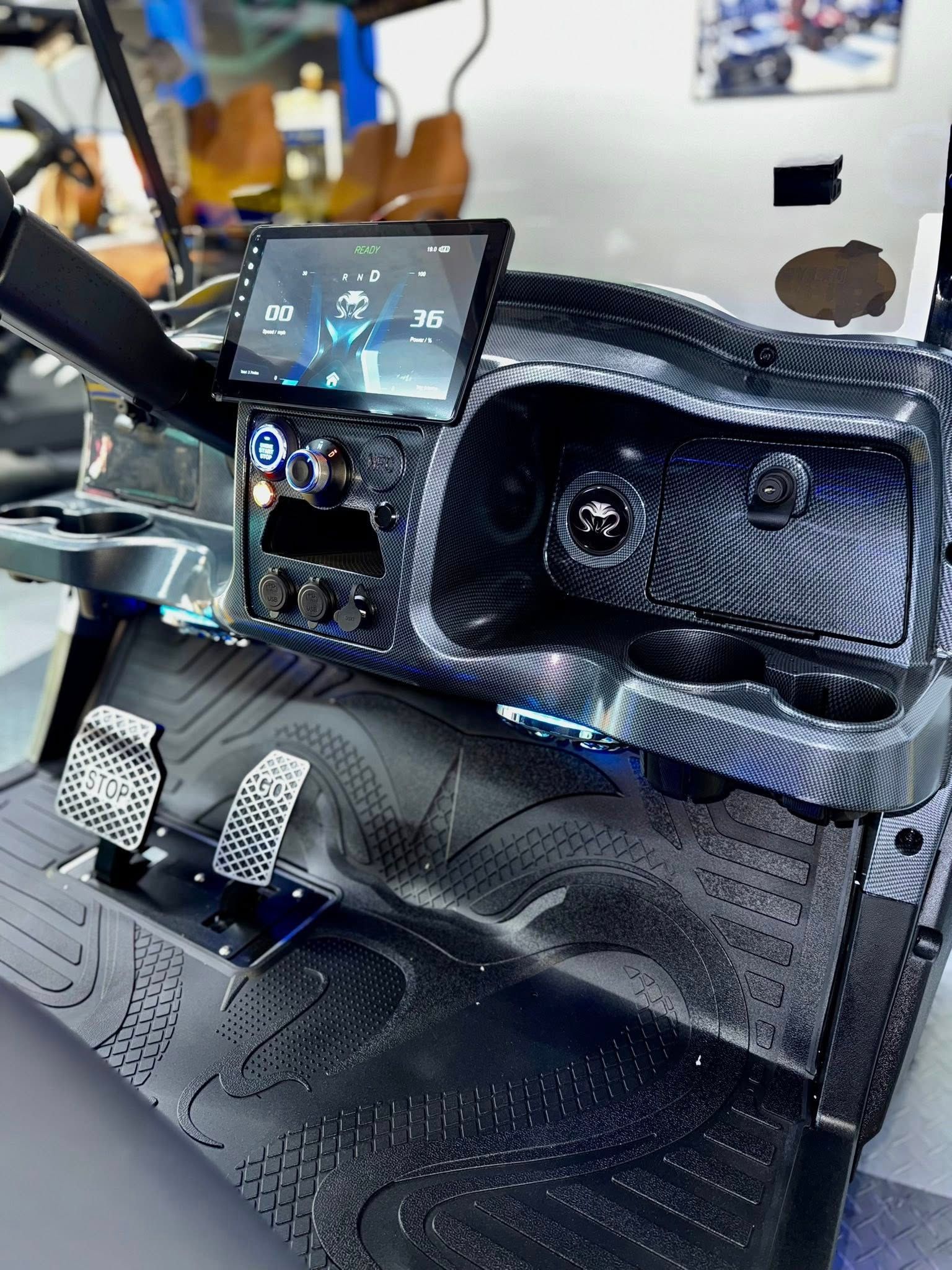 Golf cart dashboard with carbon fiber design, touchscreen, pedals, and cup holders.