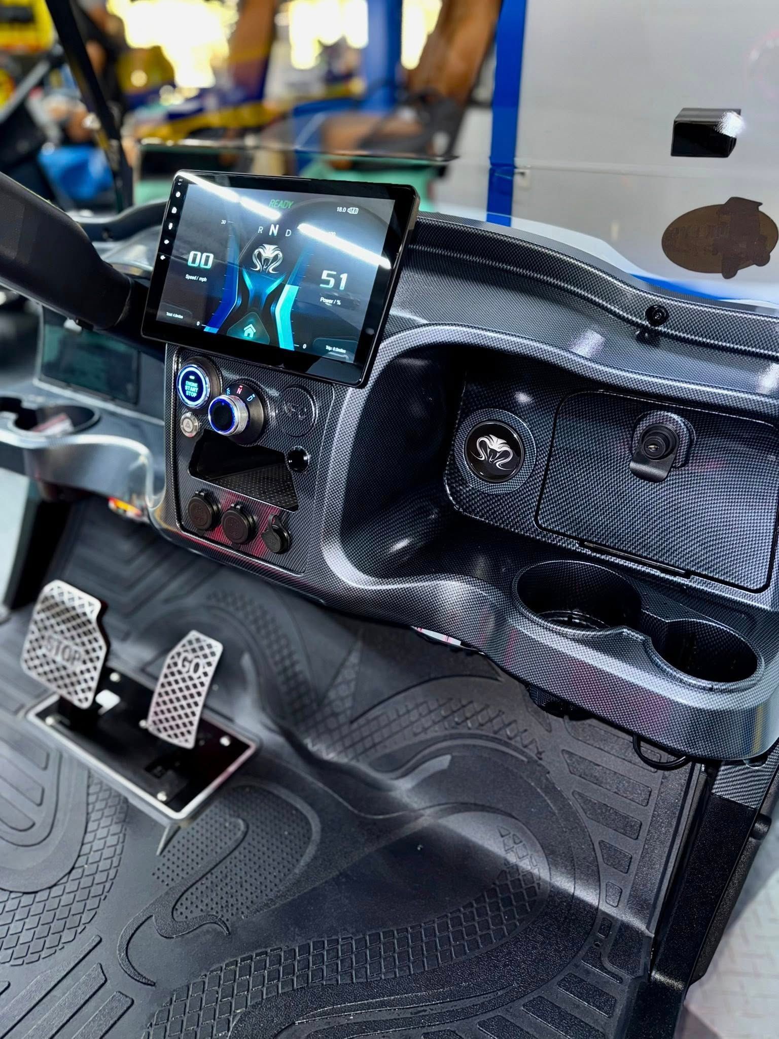 Modified golf cart dashboard with a touchscreen, cup holders, and racing pedals.