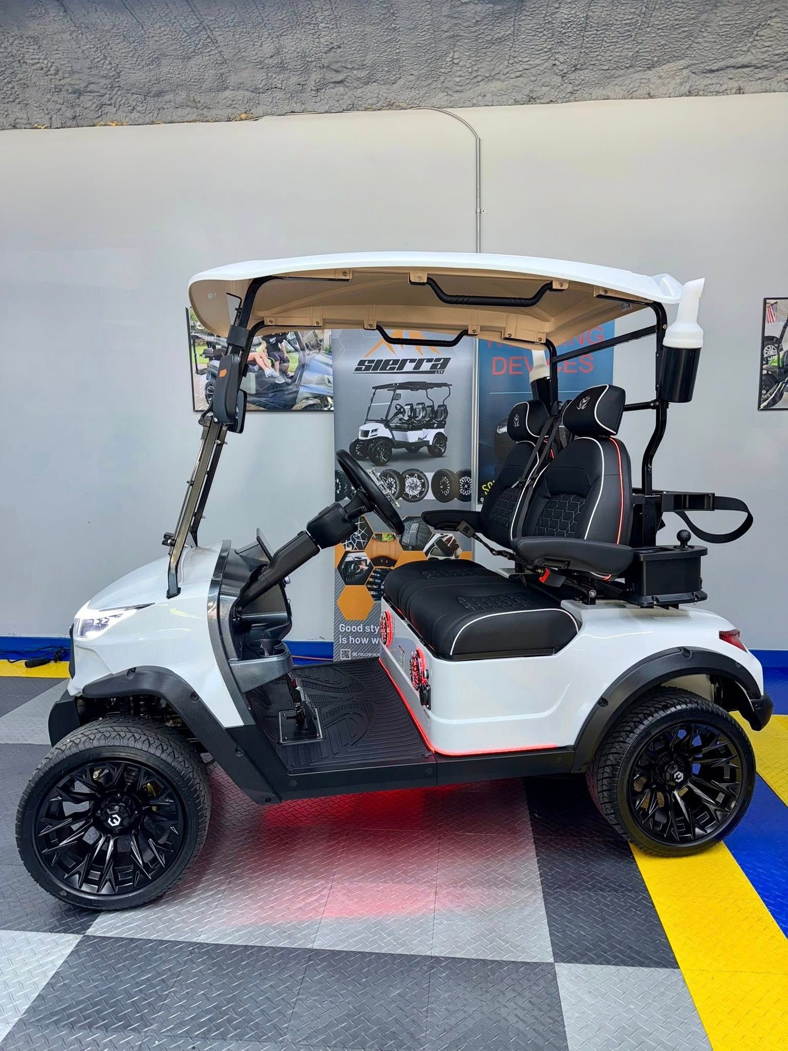 White golf cart with black wheels, black seats, and red underglow. In a showroom setting.