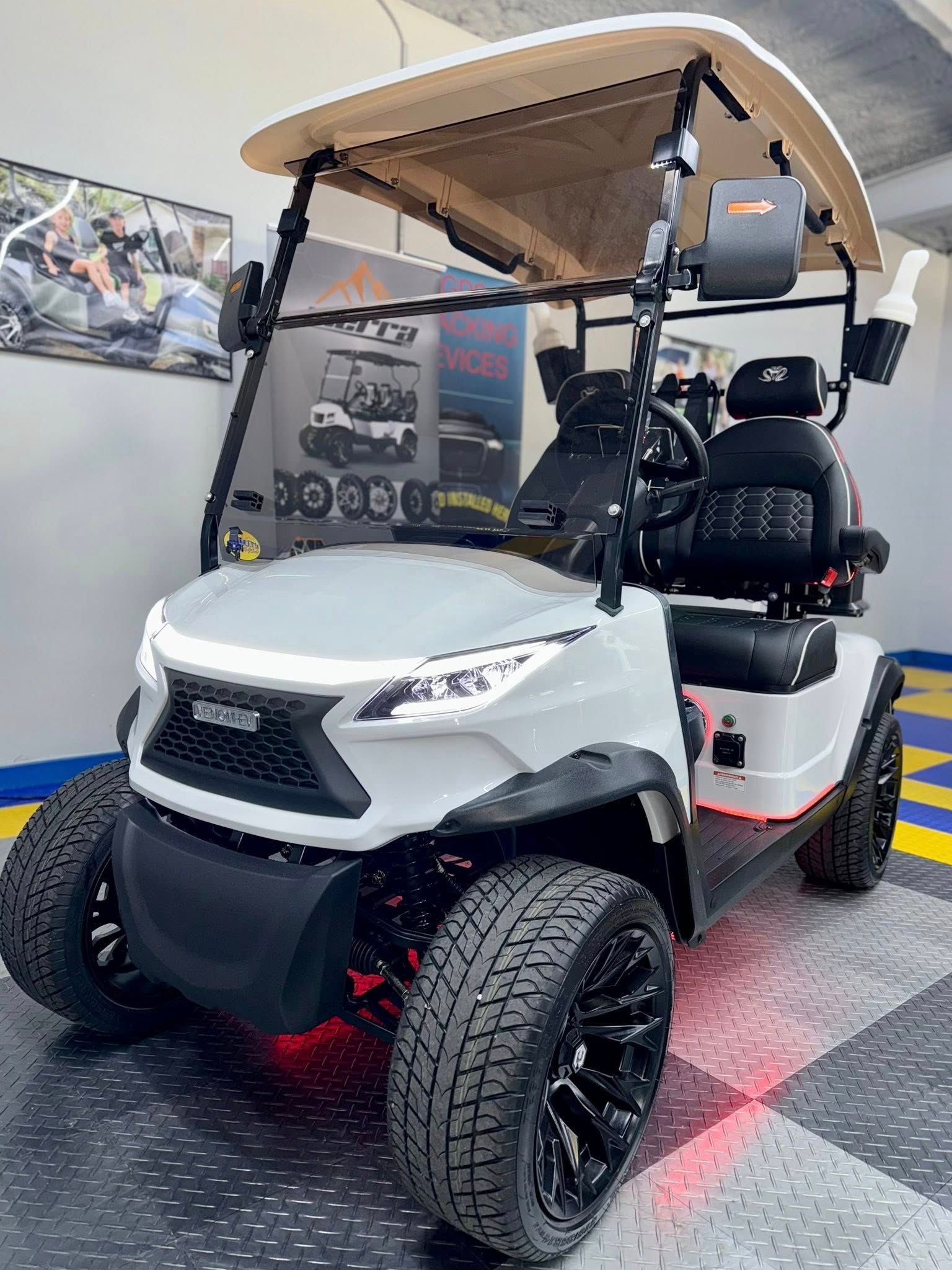 White golf cart with black accents, custom wheels, LED lights, tan roof, indoors.