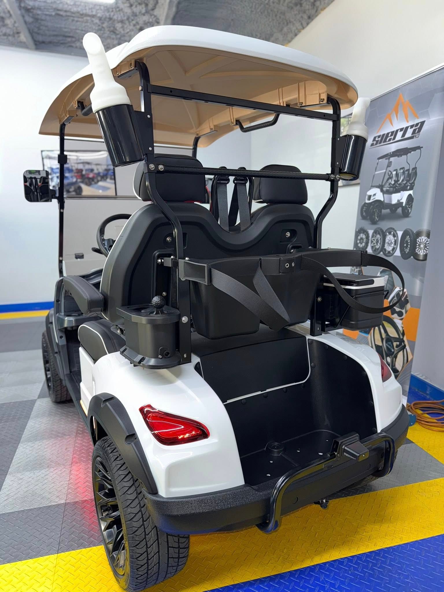 White and black golf cart with large tires and sound system, indoors.