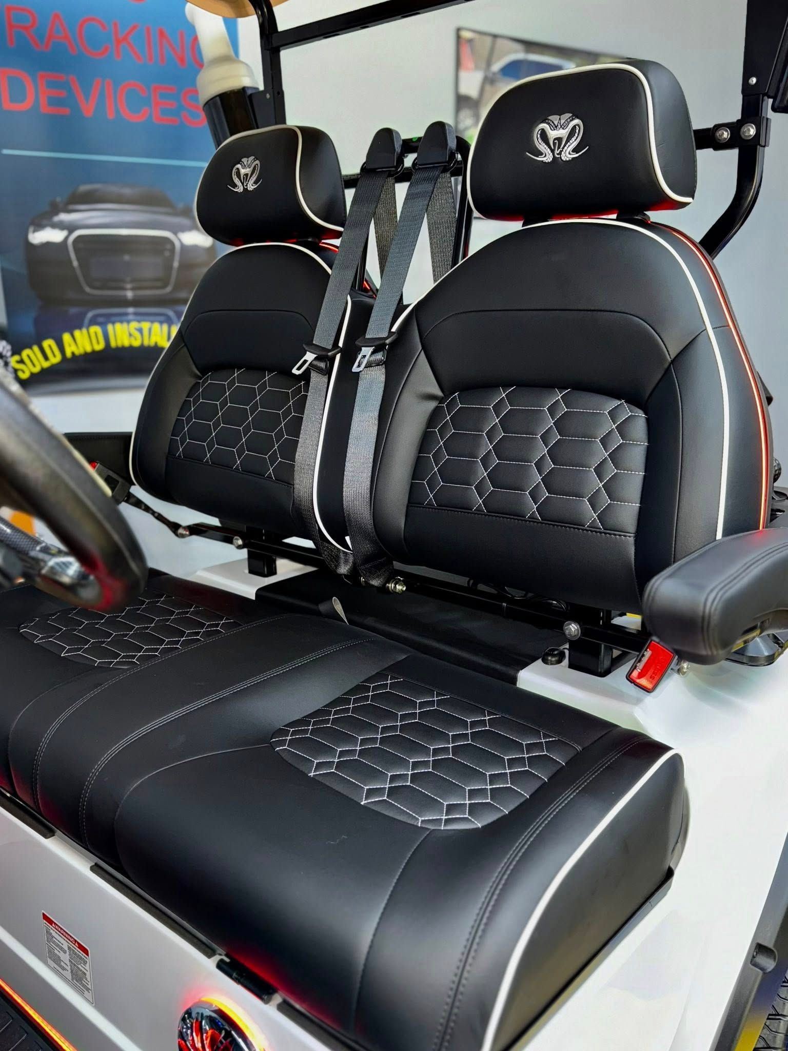 Golf cart seats with black and white leather and safety belts.