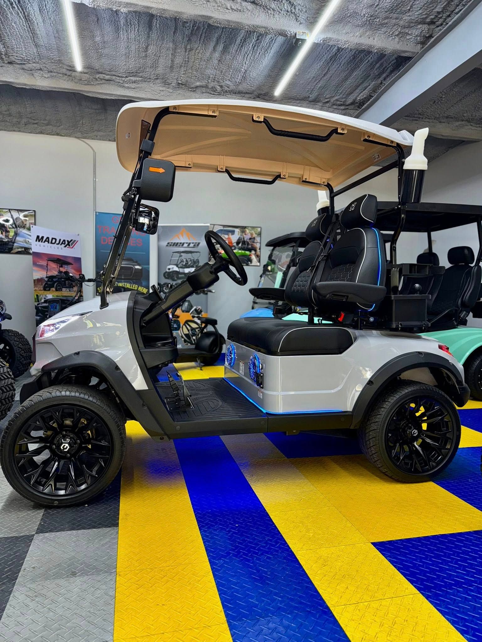 Gray golf cart with black wheels and seats, beige roof, parked on blue and yellow floor.