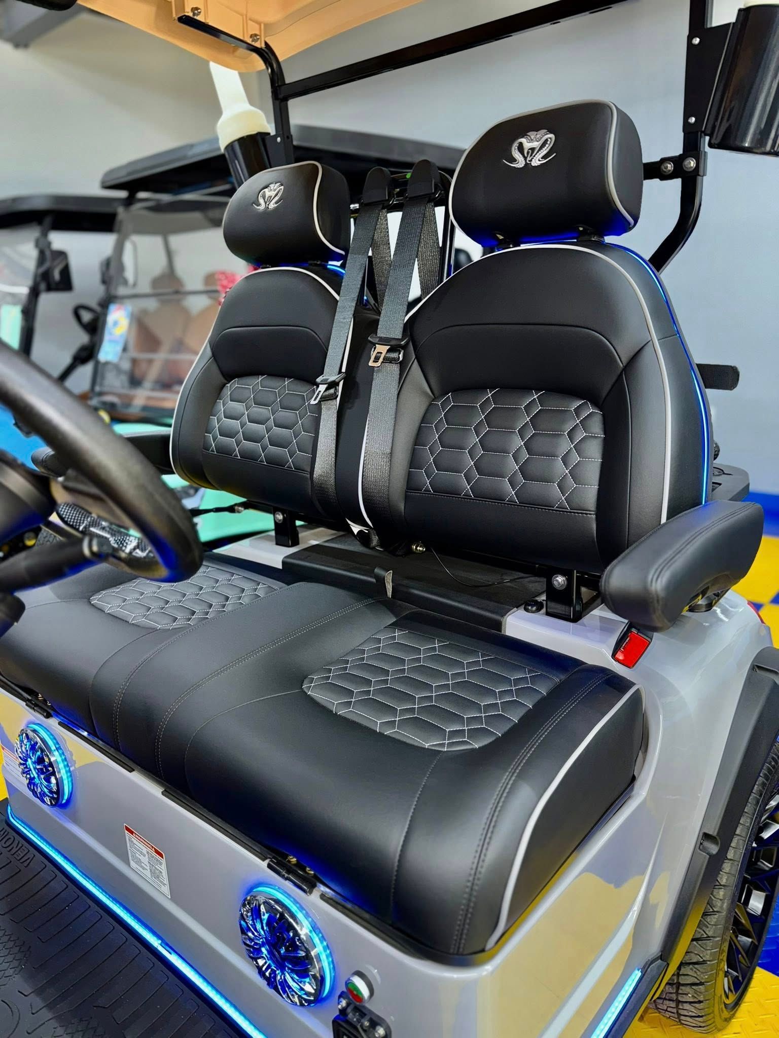 Gray golf cart interior with black and white upholstered seats, armrests, and headrests; blue accent lights.