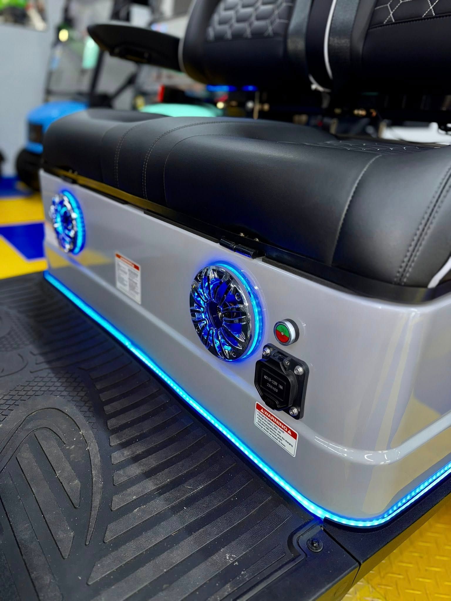 Silver golf cart rear storage box with blue LED lights, speakers, and power outlet.