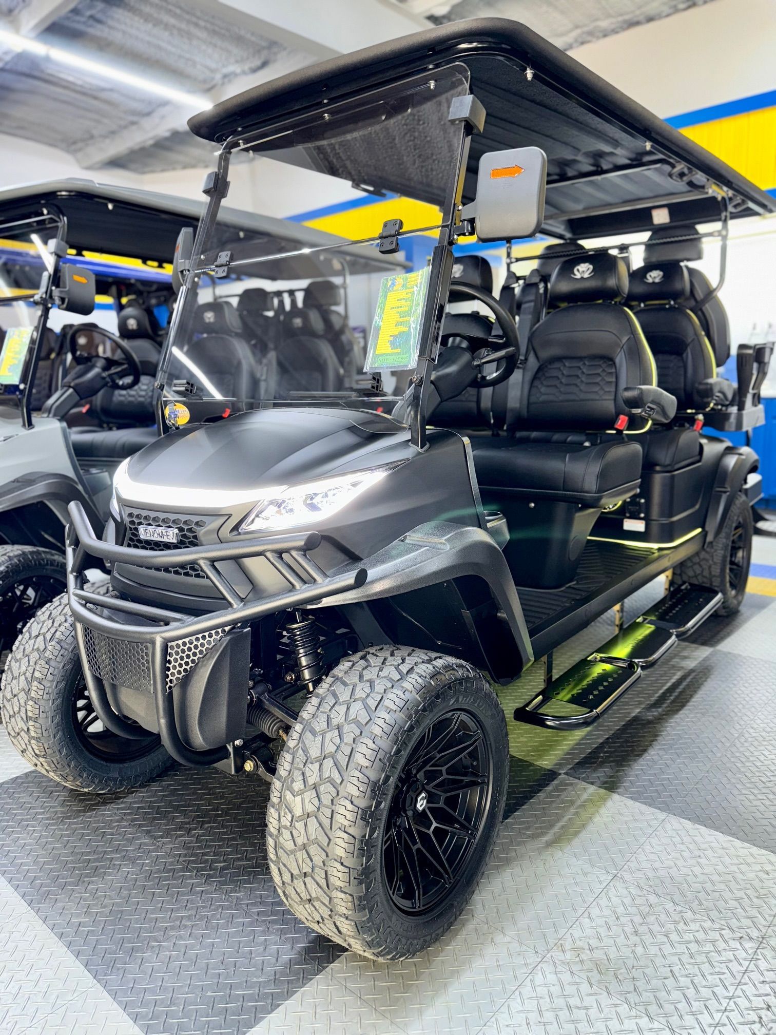 Black golf cart with black wheels, seats, and canopy, on a showroom floor.