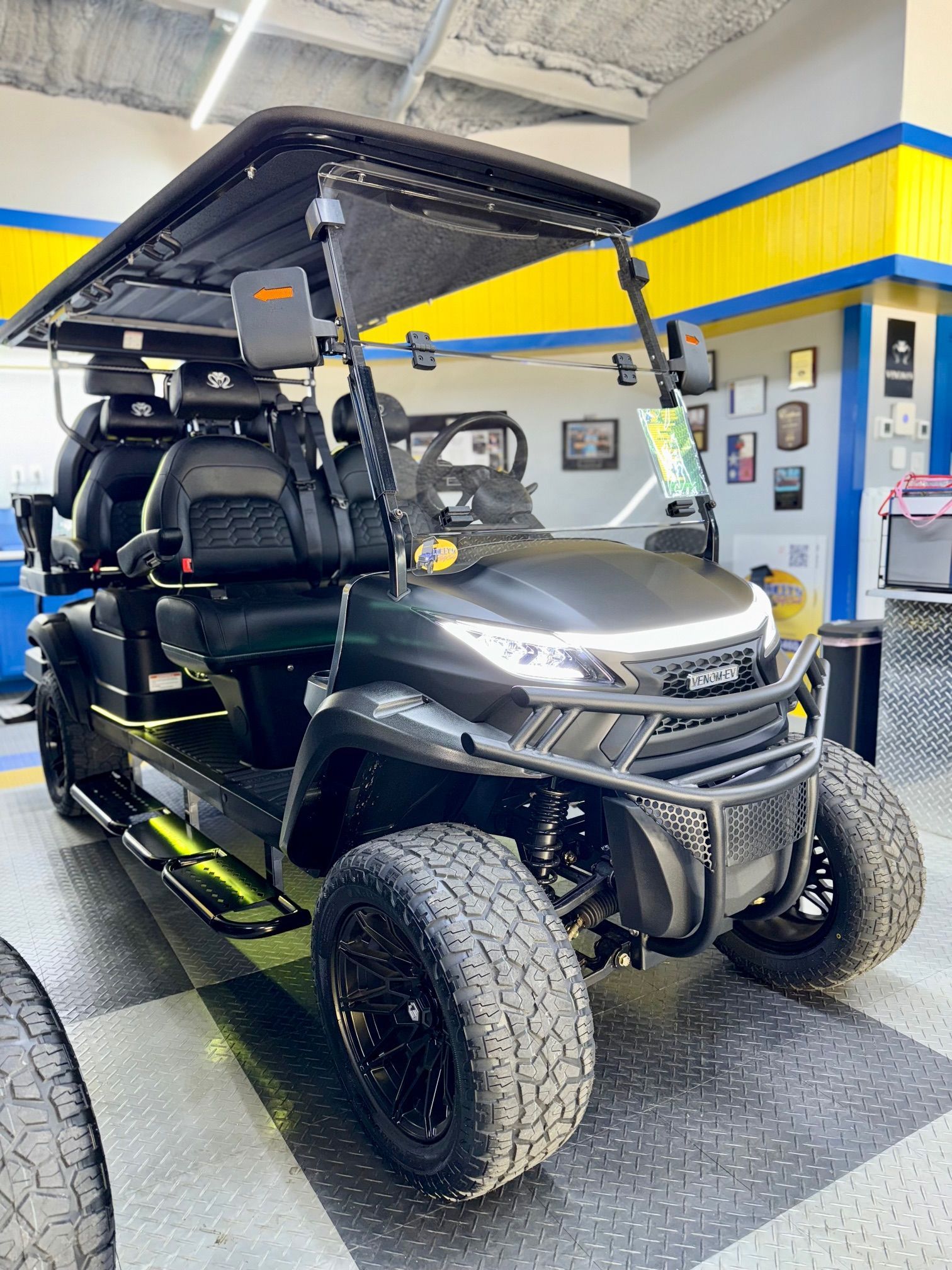 Black golf cart with lifted suspension, black wheels, and off-road tires. Inside a garage.
