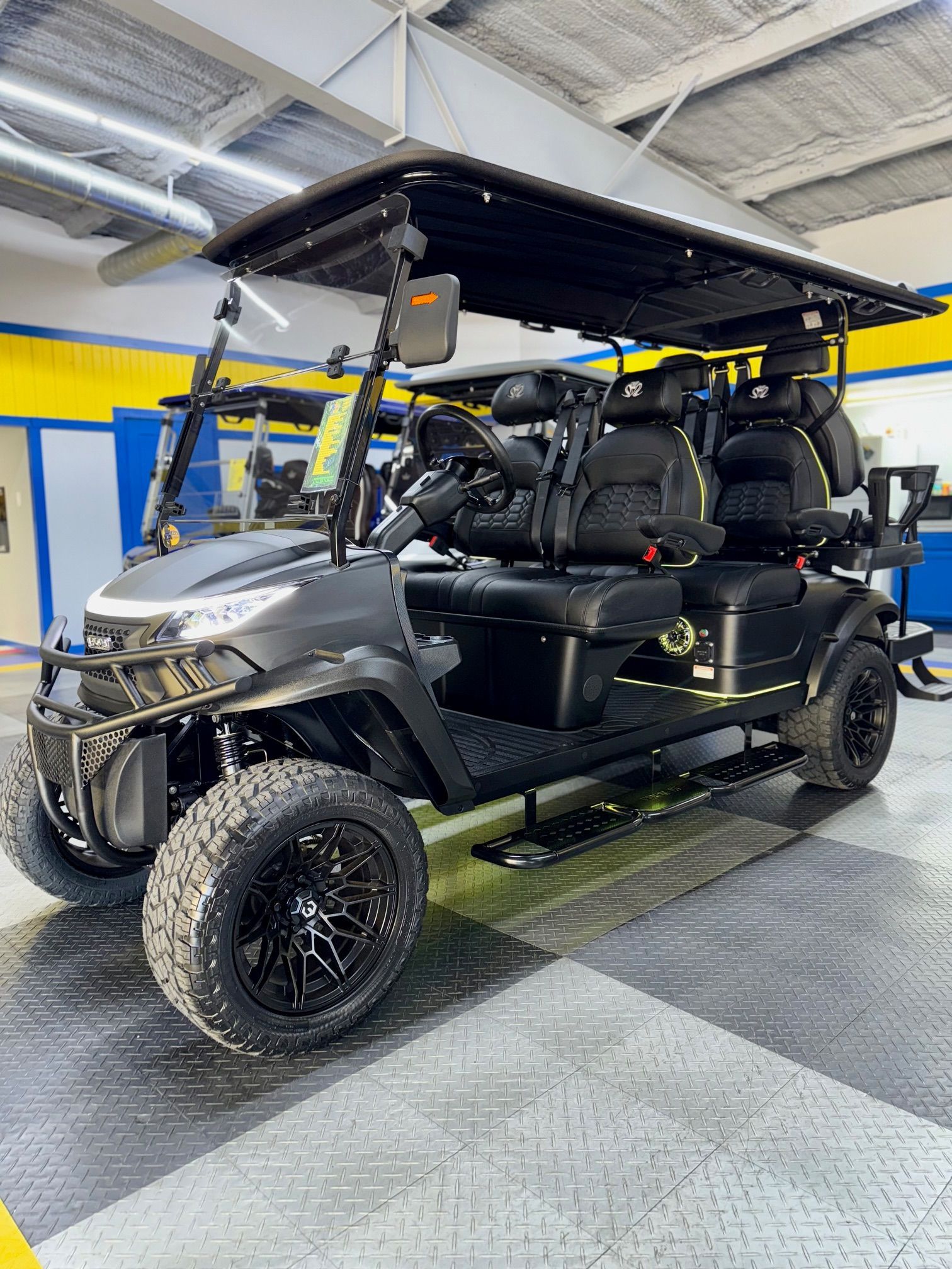 Black golf cart with off-road tires, a canopy, and four seats, parked indoors on a tiled floor.