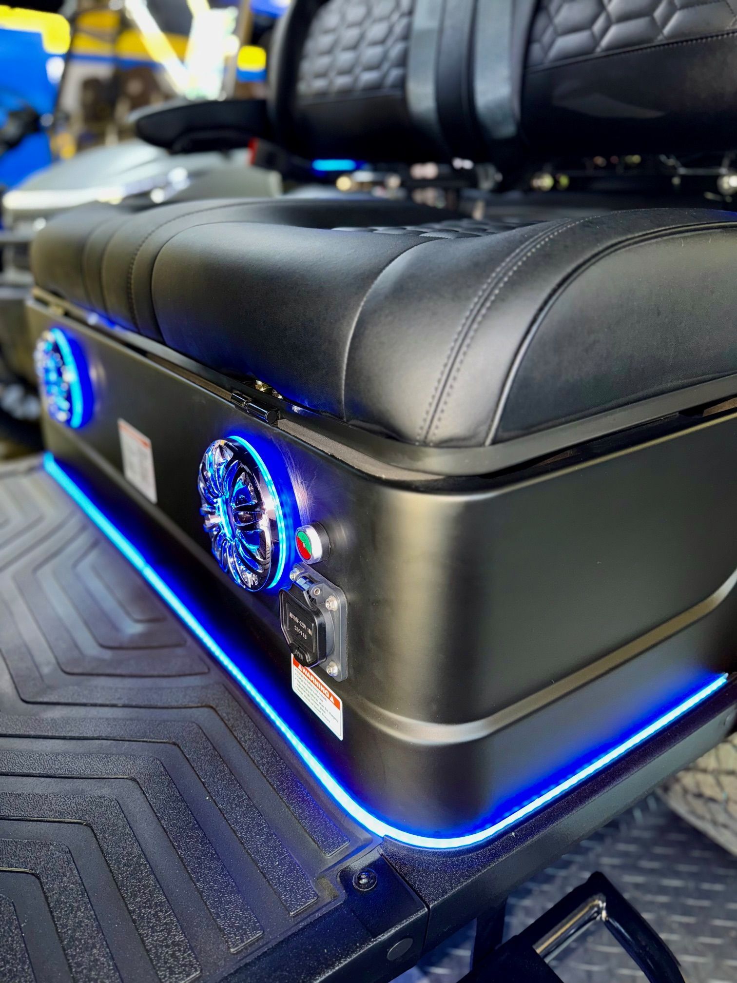 Black seat base with blue LED lights, speakers, and power outlet on a vehicle.