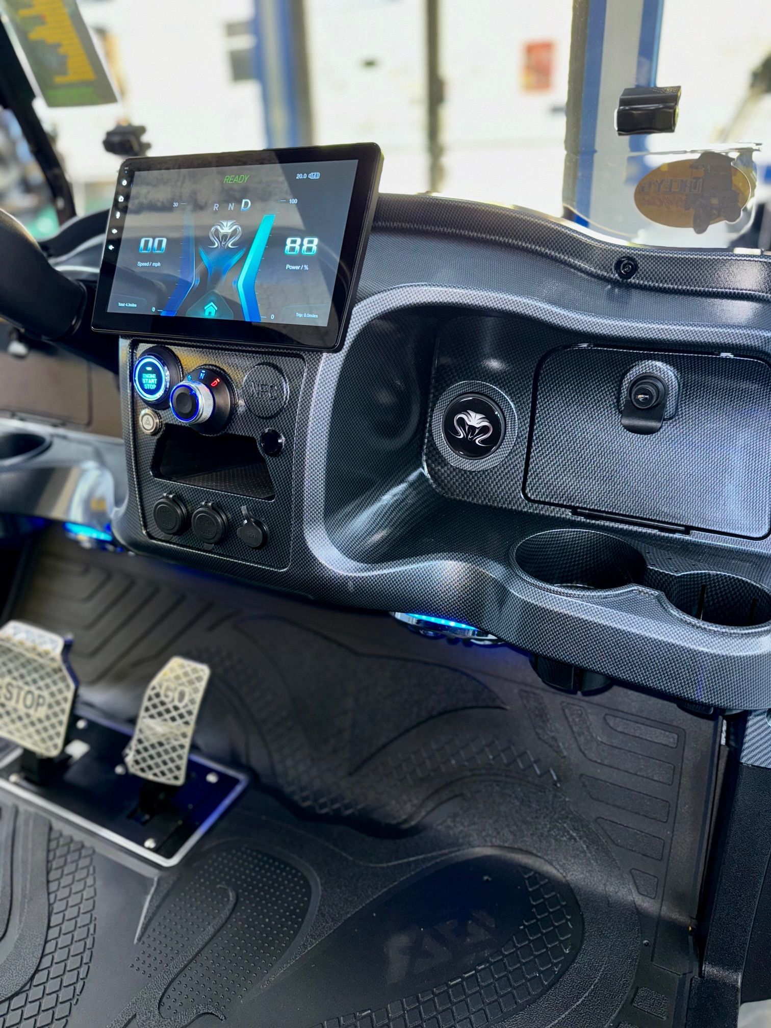 Golf cart dashboard with a digital display, cupholders, and carbon fiber accents.
