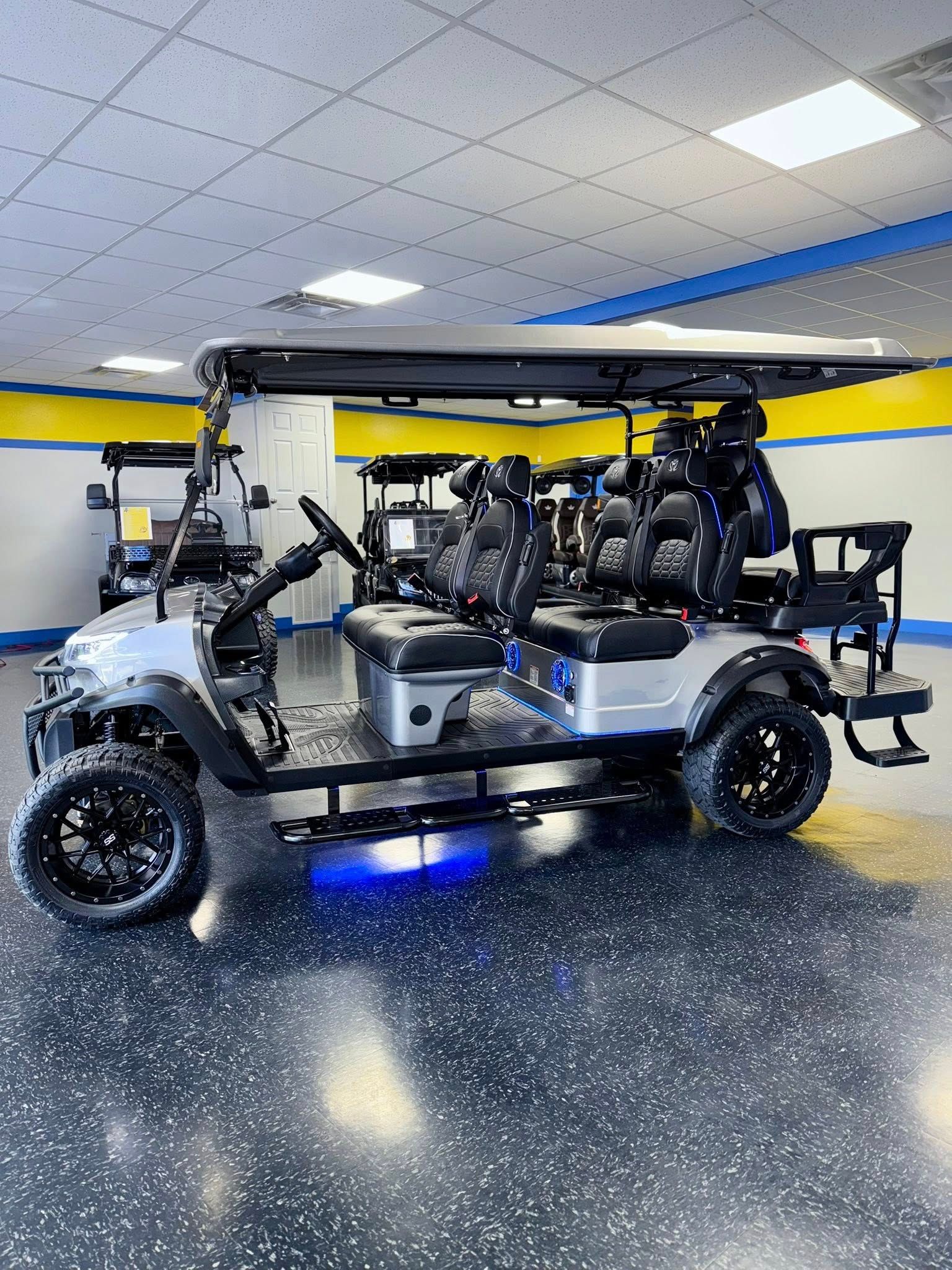 Silver golf cart with black wheels and roof, six seats, in a showroom.