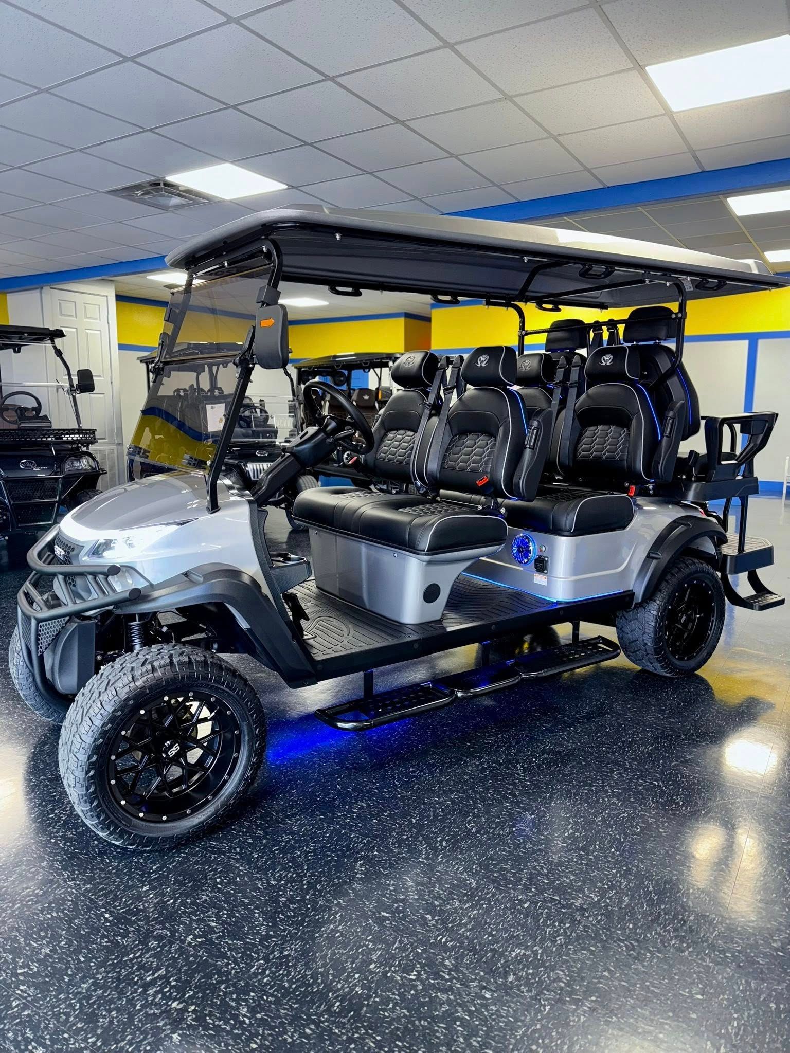 Silver custom golf cart with black accents, lifted wheels, LED lights, indoor setting.