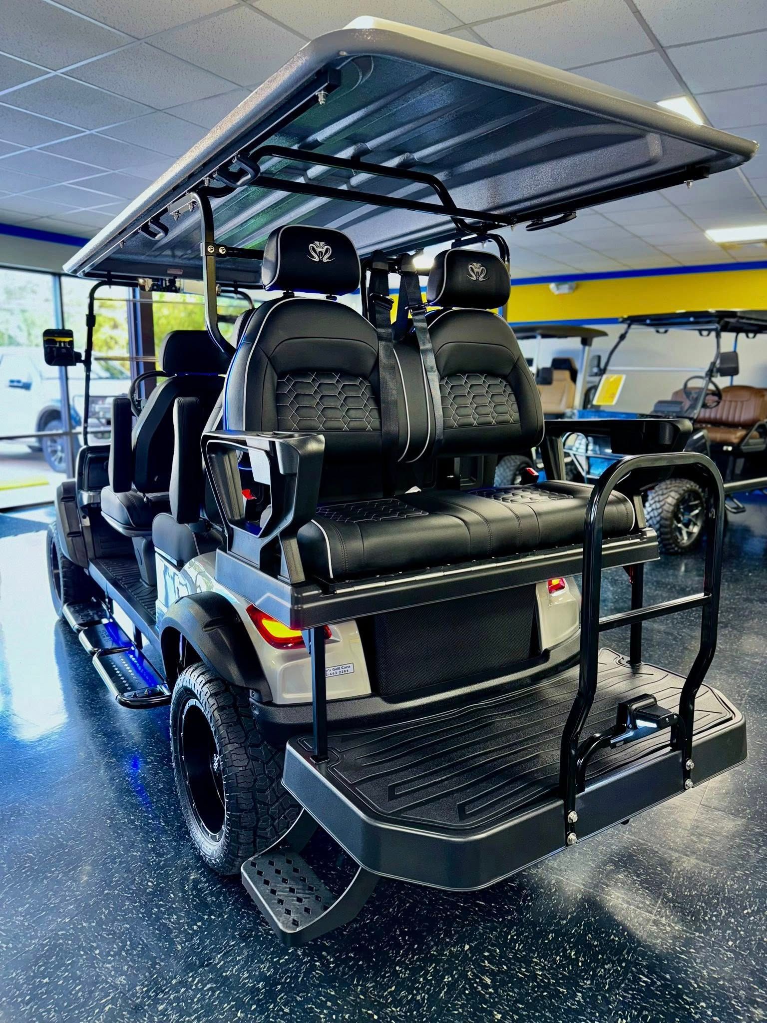 A luxury golf cart, black and blue, with rear seating, and a sunshade in an auto shop.