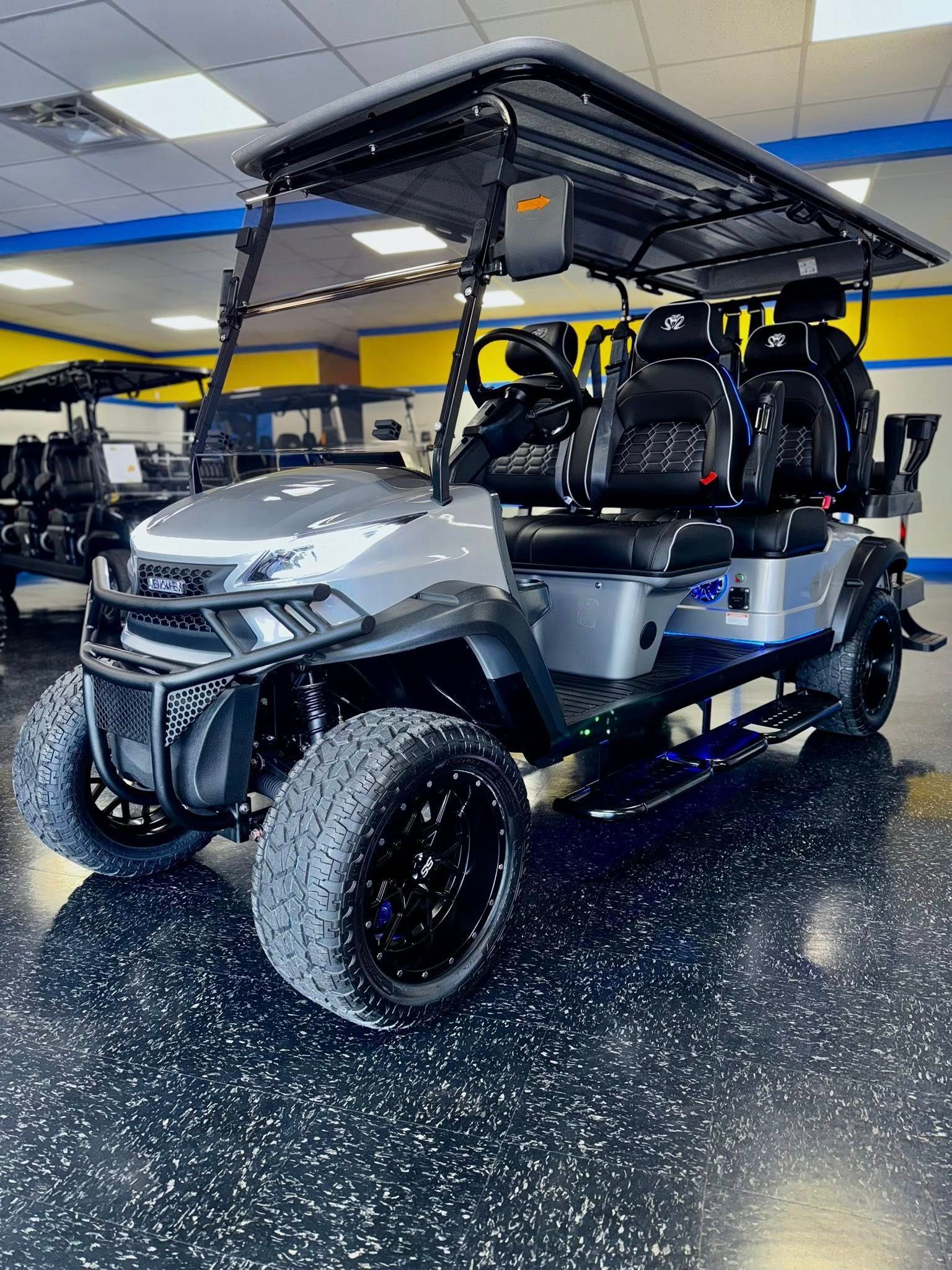 Gray lifted golf cart with black wheels, seats, and roof, indoors.