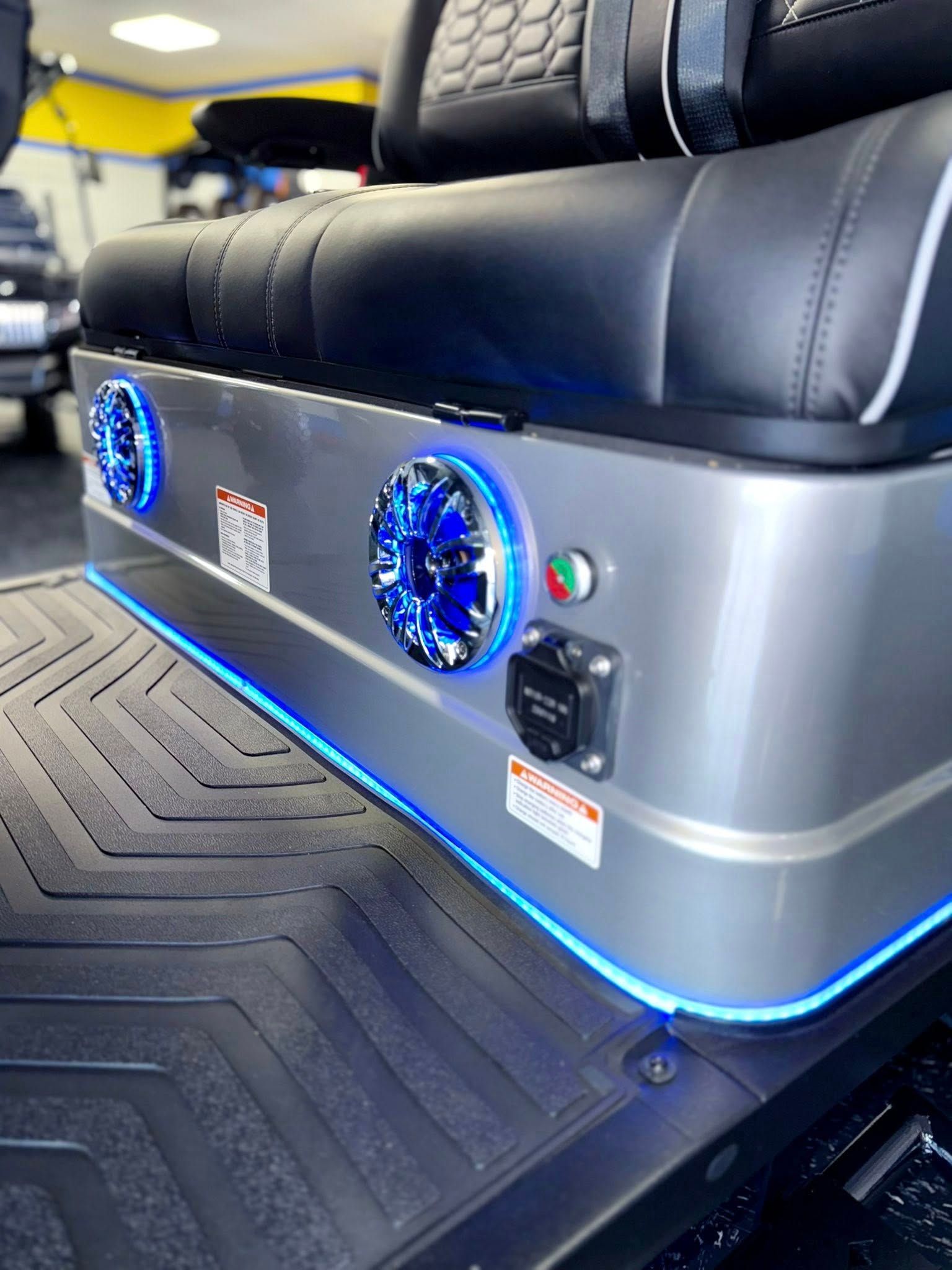 Close-up of a golf cart's silver base with blue LED lights, speakers, and a power outlet.