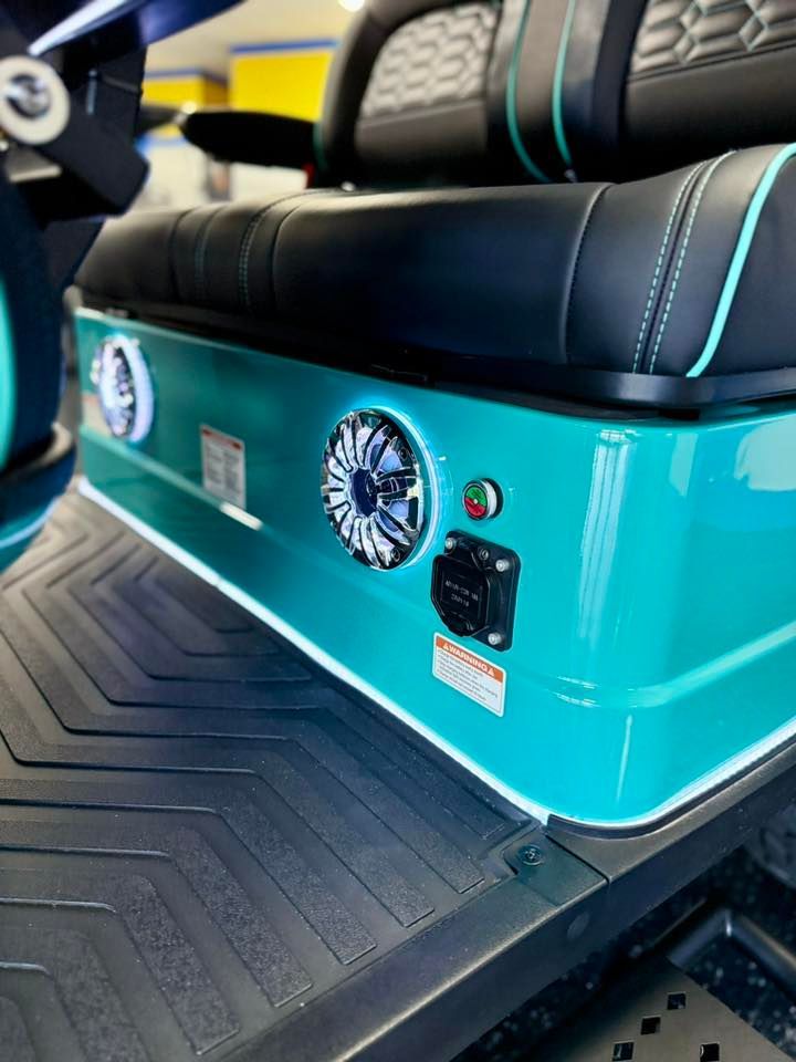 Teal golf cart seating with built-in speakers, power outlet, and LED lighting.
