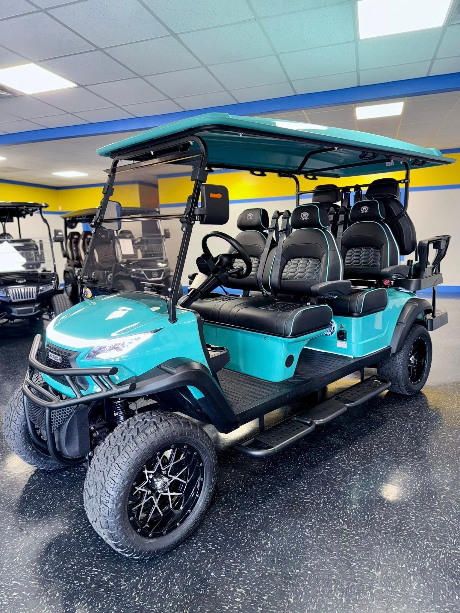 Turquoise golf cart with black accents, black wheels, and a black interior, inside a showroom.
