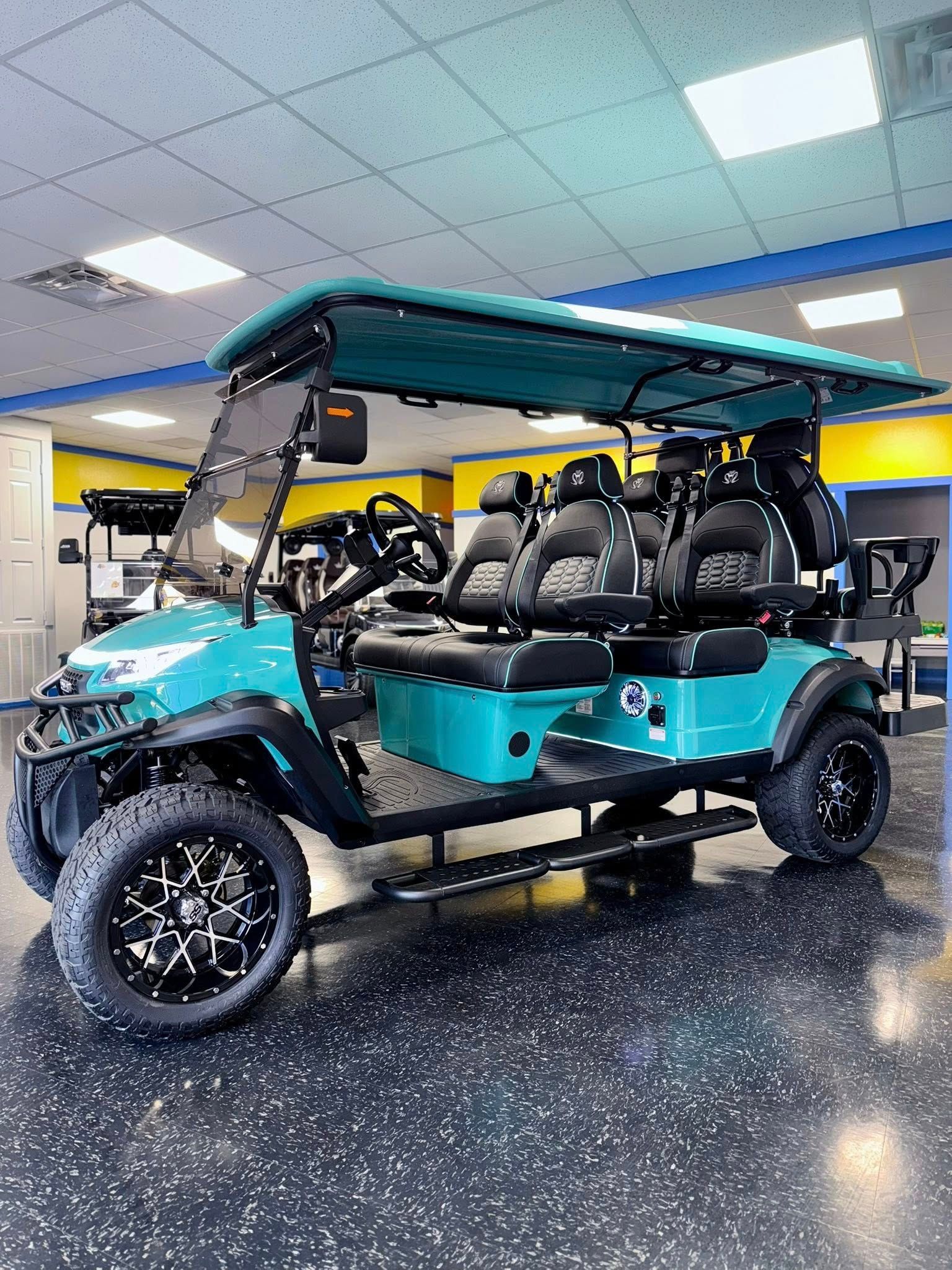 Teal six-seater golf cart with black wheels and seats, parked indoors.
