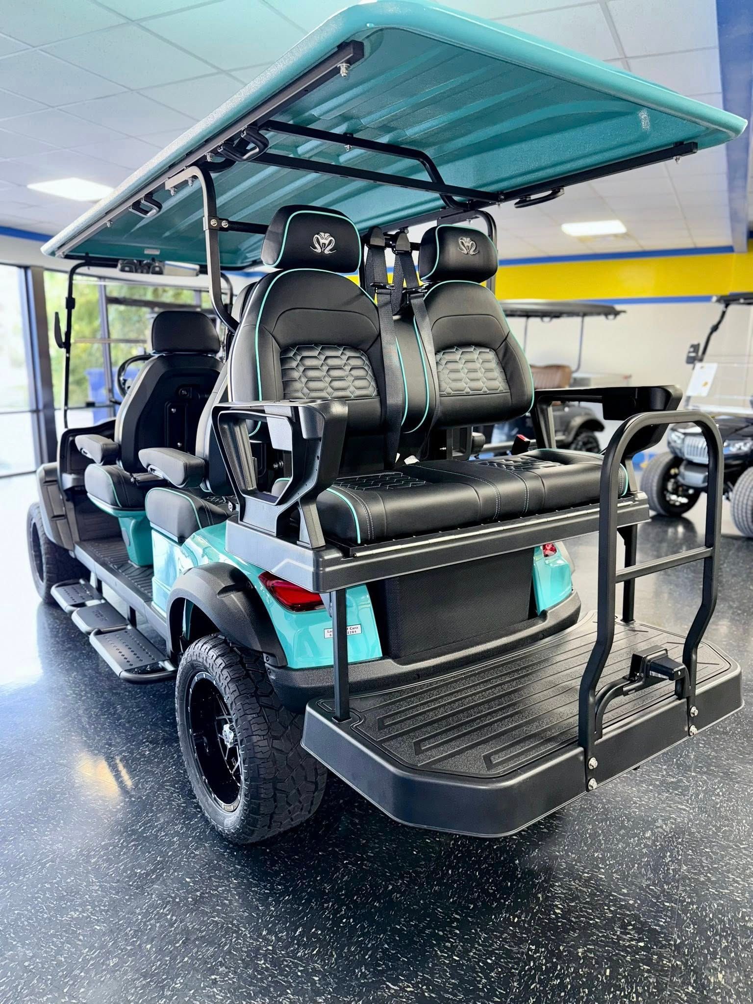 Aqua golf cart with black seats, wheels, and accents. Rear step and bench. Indoor setting.