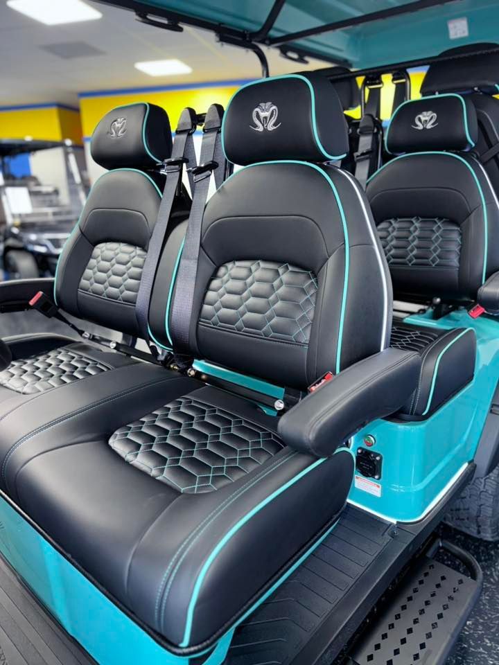 Black and teal golf cart seats with quilted detailing and headrests, in a brightly lit showroom.