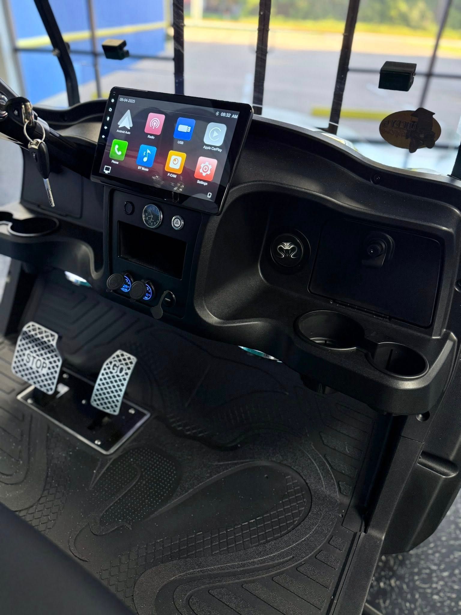 Black golf cart dashboard with a touchscreen, cup holders, and pedals.