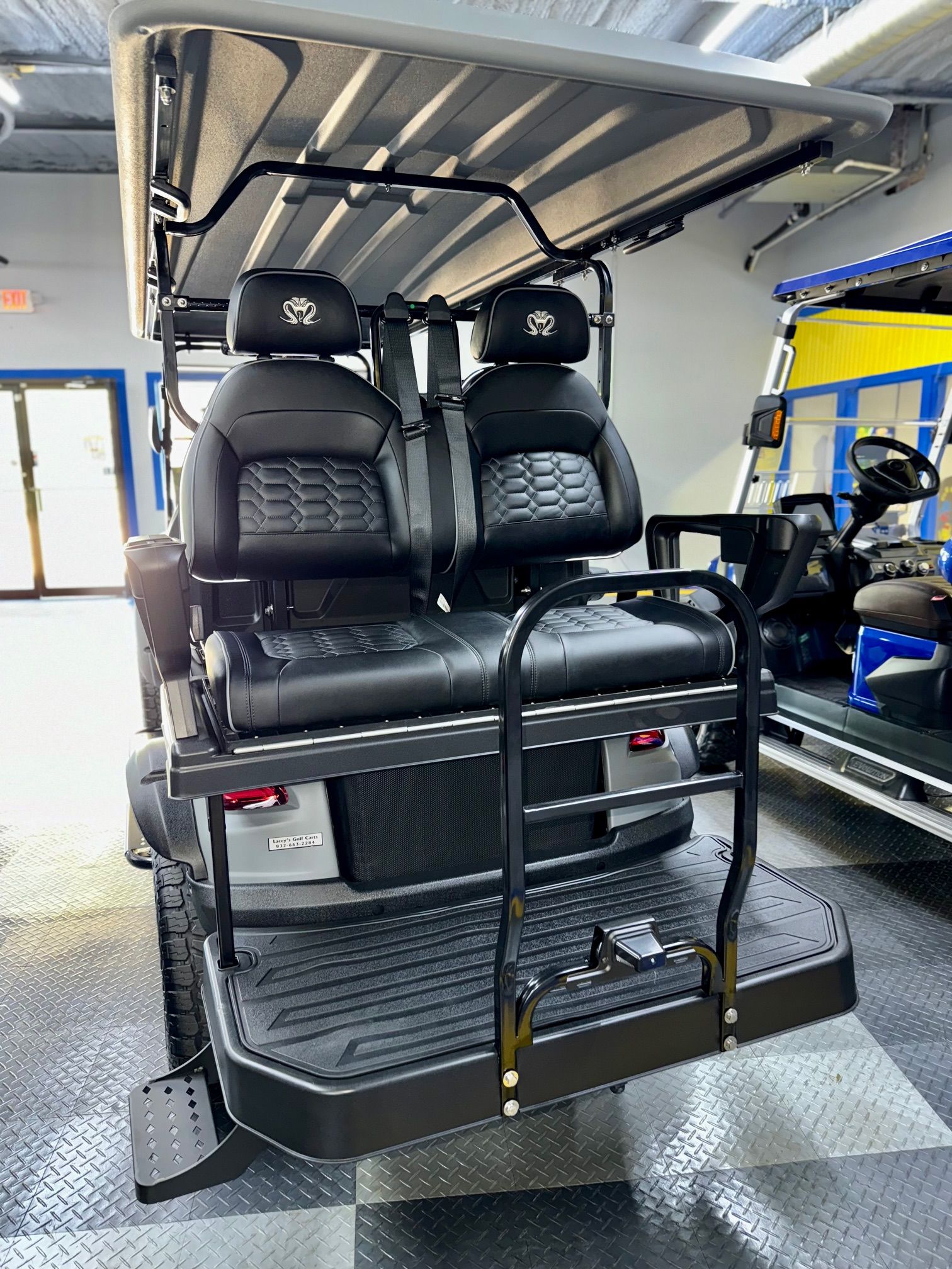 Golf cart, rear view. Black seats and frame, silver body, black diamond plate floor.