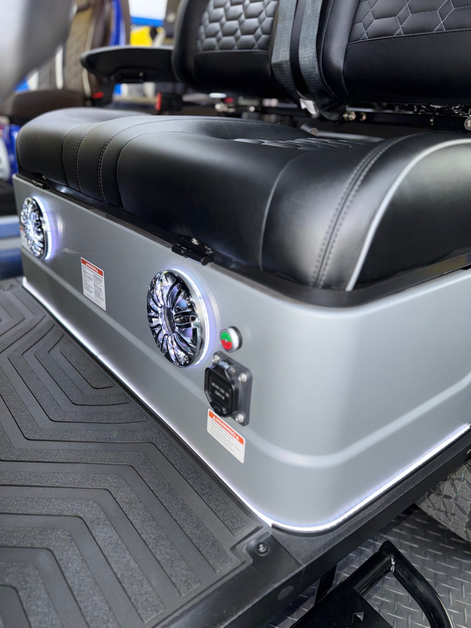 Close-up of a silver golf cart seat base with speakers, controls, and a black and gray cushioned seat.