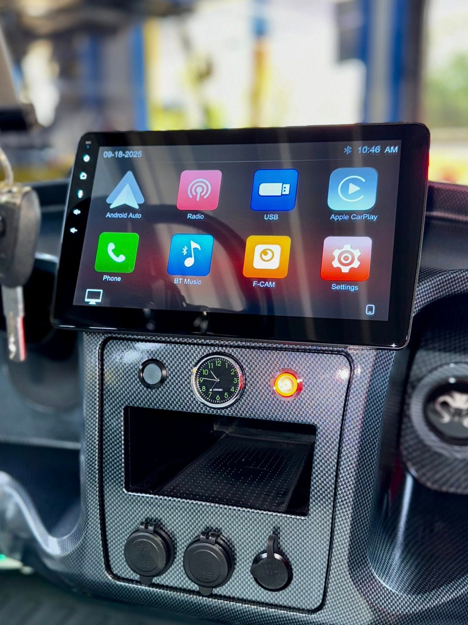 Car dashboard with a large touchscreen displaying apps. Black and silver accents, visible charging ports.