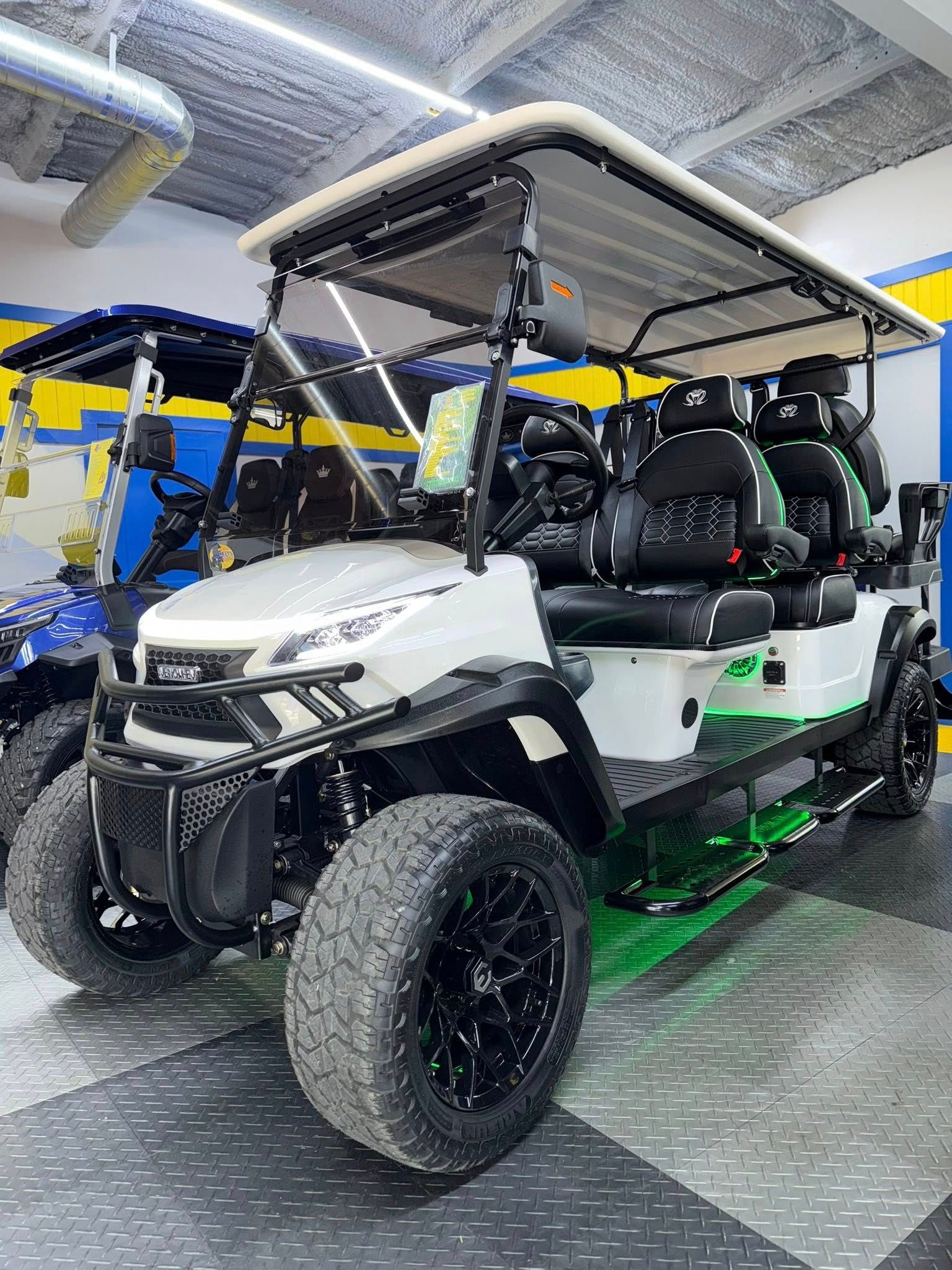 White and green lifted golf cart with black wheels, seats and details parked indoors.