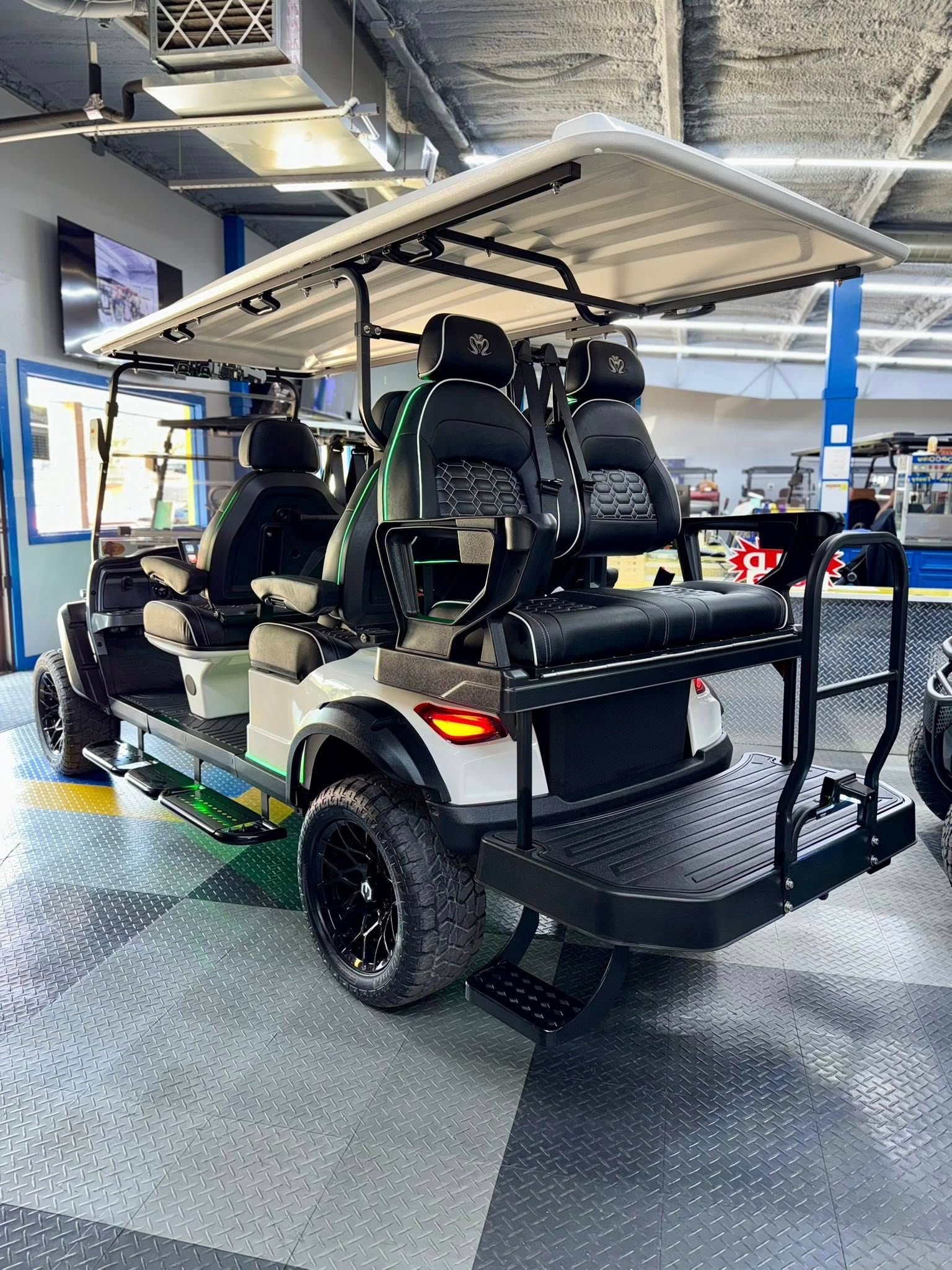 White golf cart with black seats, wheels, and rear platform, in a garage.