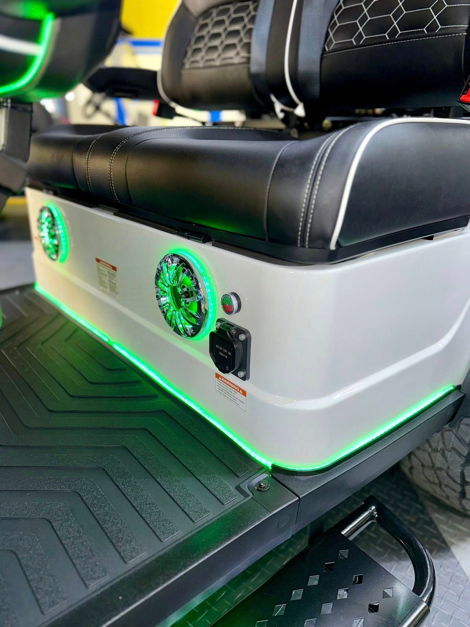 Close-up of a silver golf cart seat with green accent lighting and speakers.