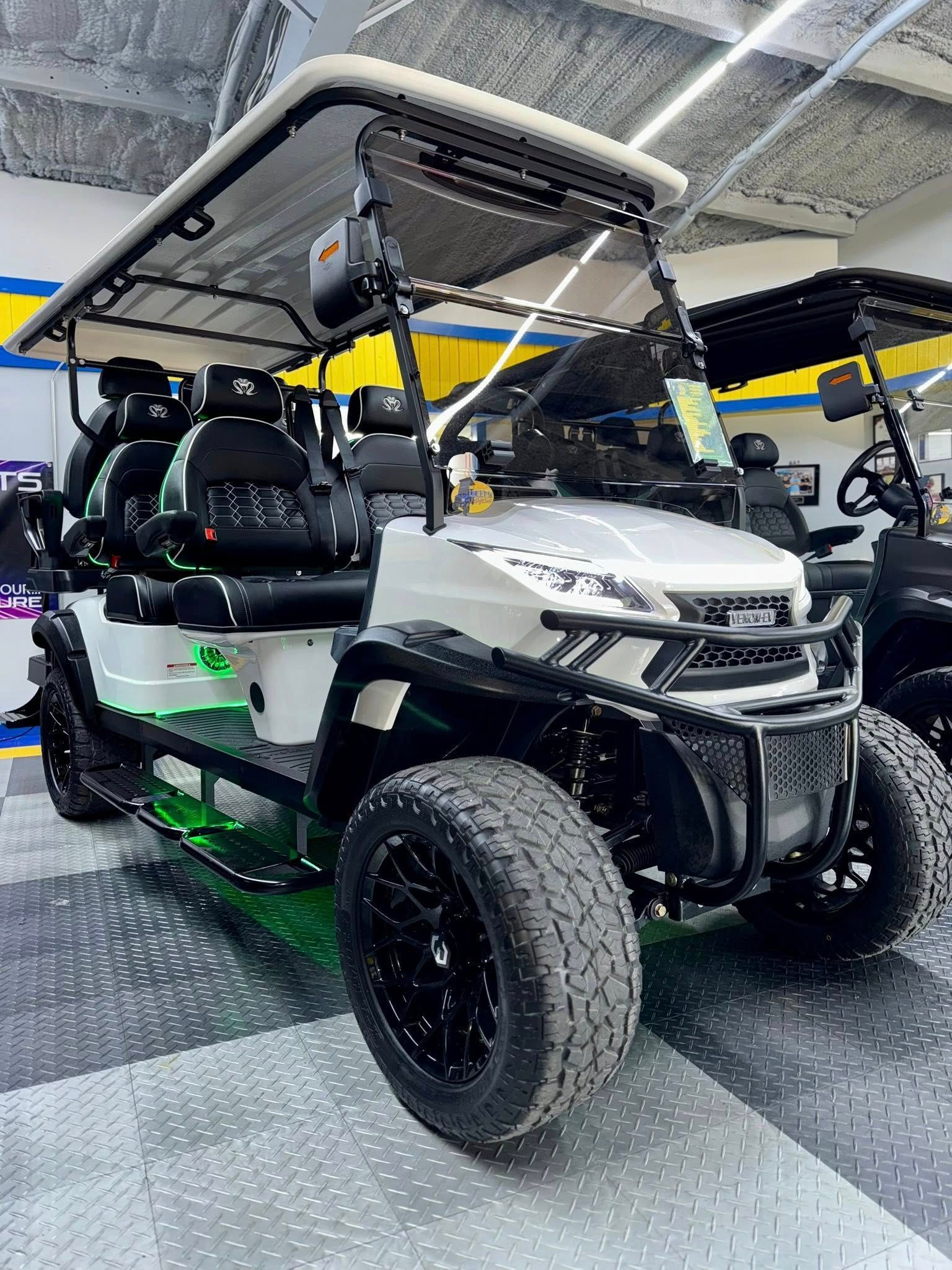 White and green golf cart with black wheels, seats, and a canopy. It is parked indoors.