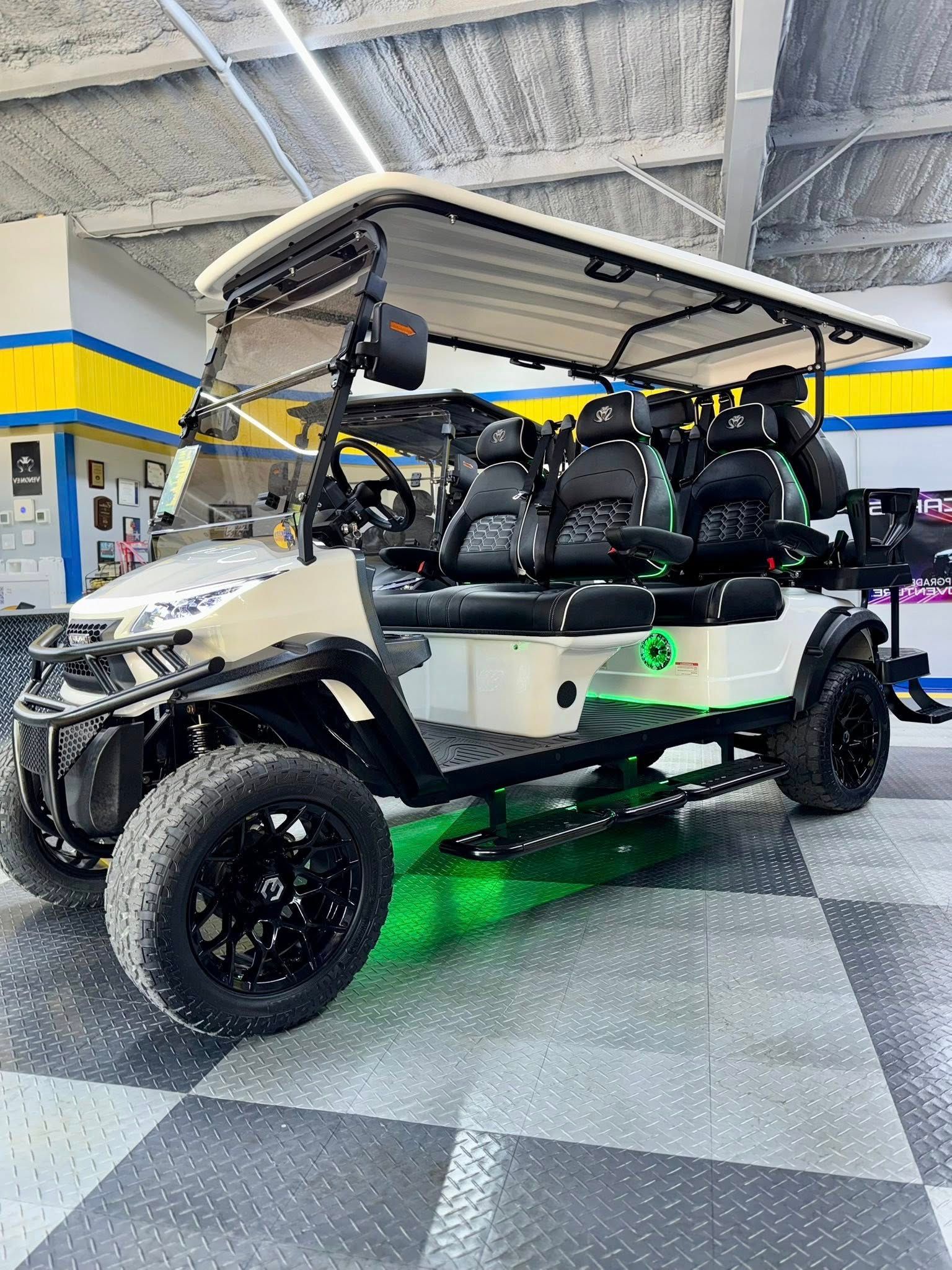 Off-white golf cart with black wheels and seating, green underglow, parked indoors.