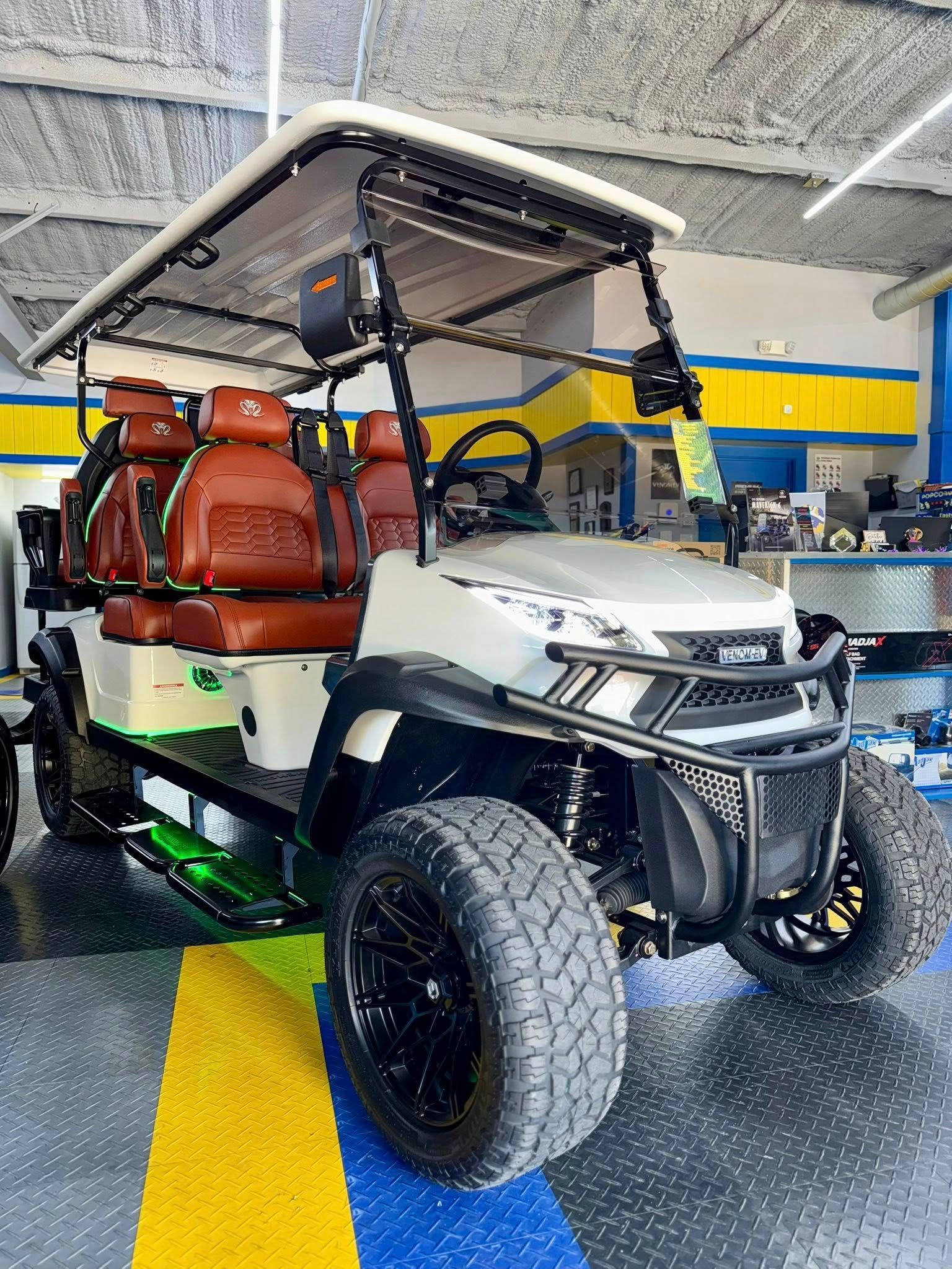 White off-road golf cart with black accents and brown seats, parked indoors.