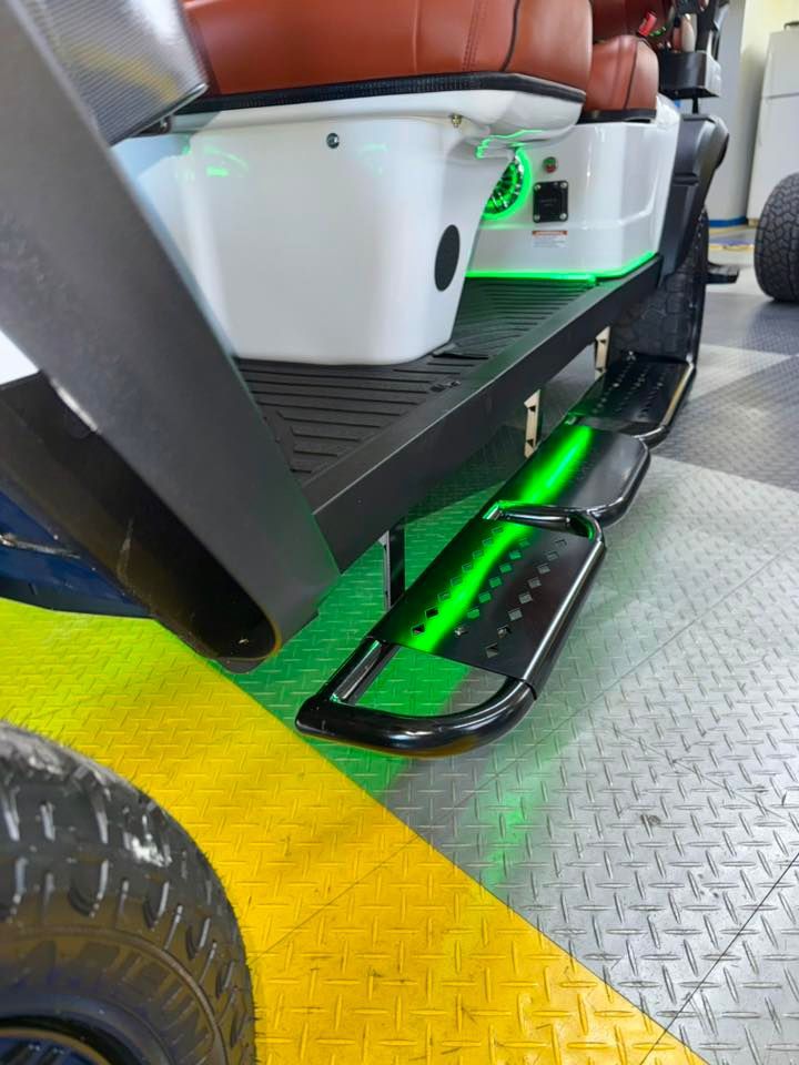 Black golf cart with green underglow, step bars, and brown seats.