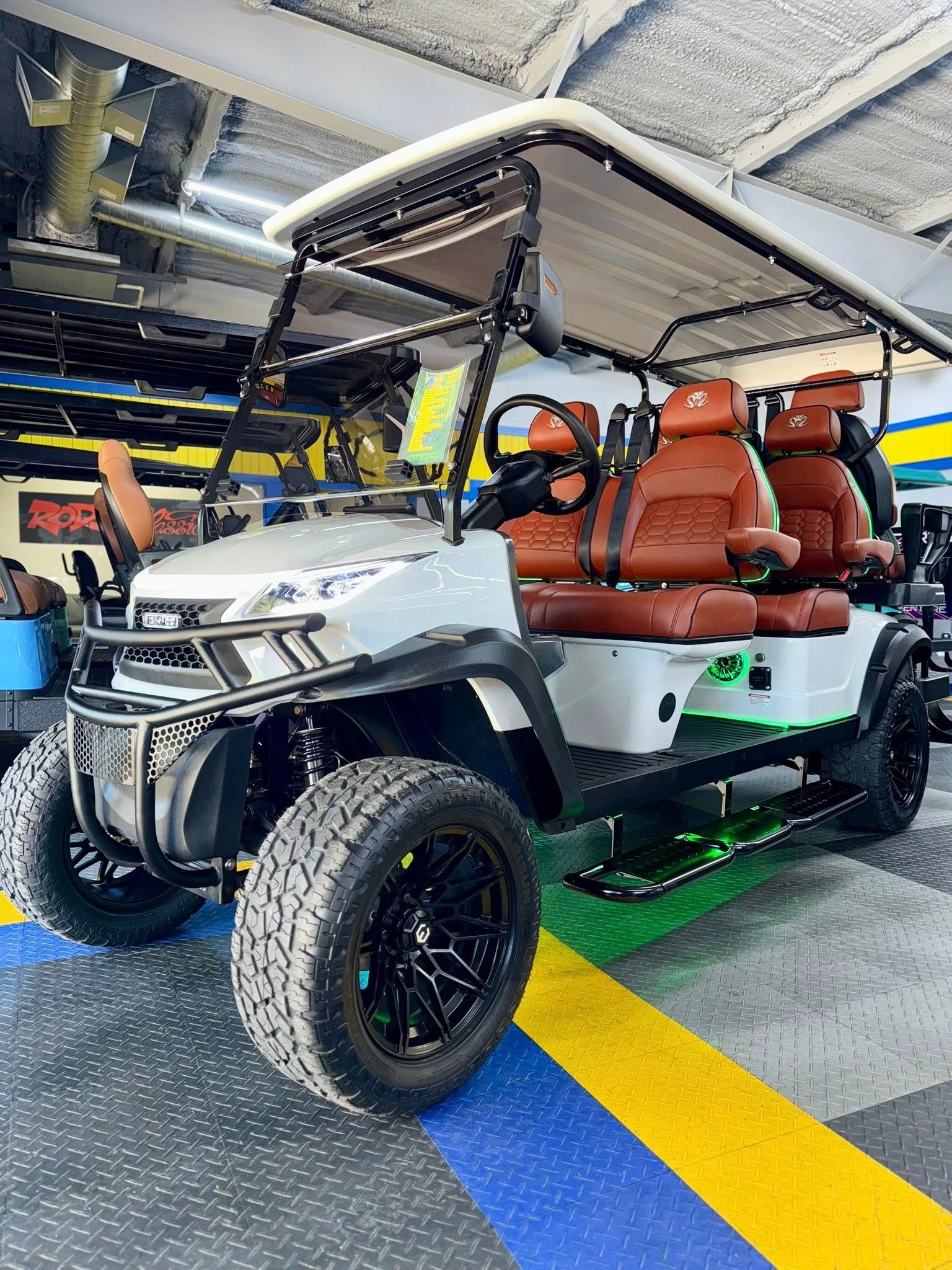 White and brown custom golf cart with black wheels, large tires, and LED lights, indoors.