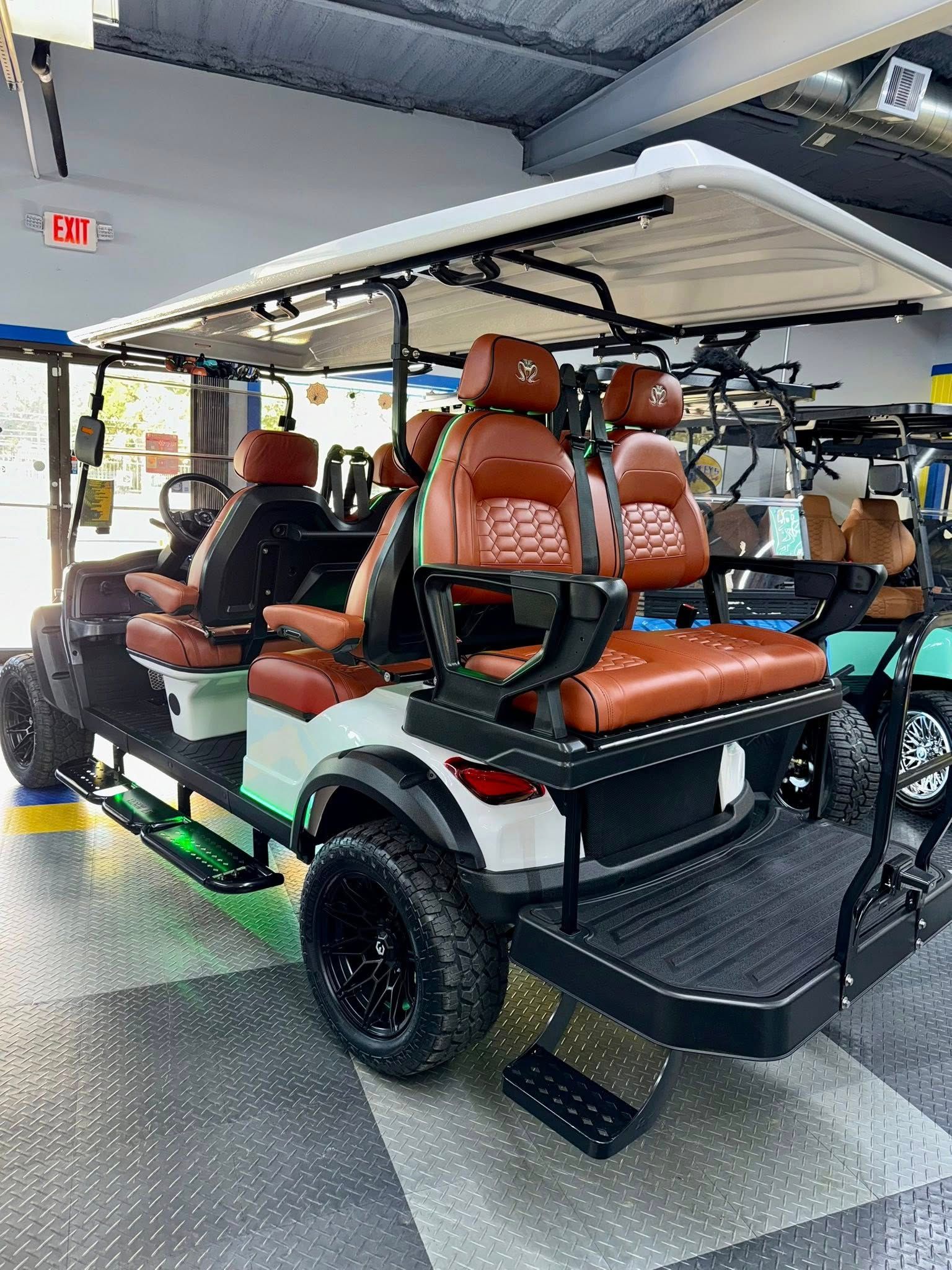 Custom six-seat golf cart with brown and white seats, black wheels, and a white roof, indoors.