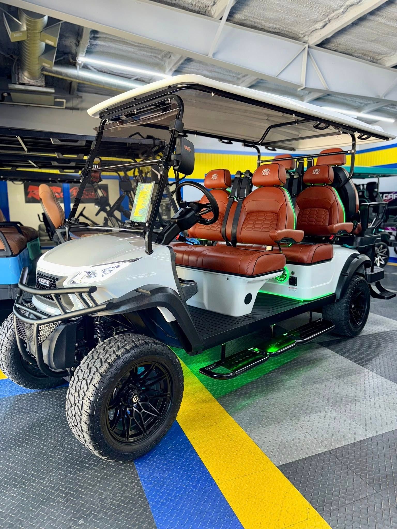 White, customized golf cart with brown seats, black wheels, and green underglow, in a showroom.