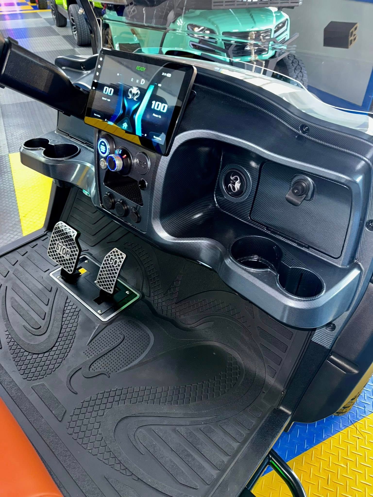 Golf cart dashboard with a large touchscreen display, cup holders, pedals, and black textured interior.
