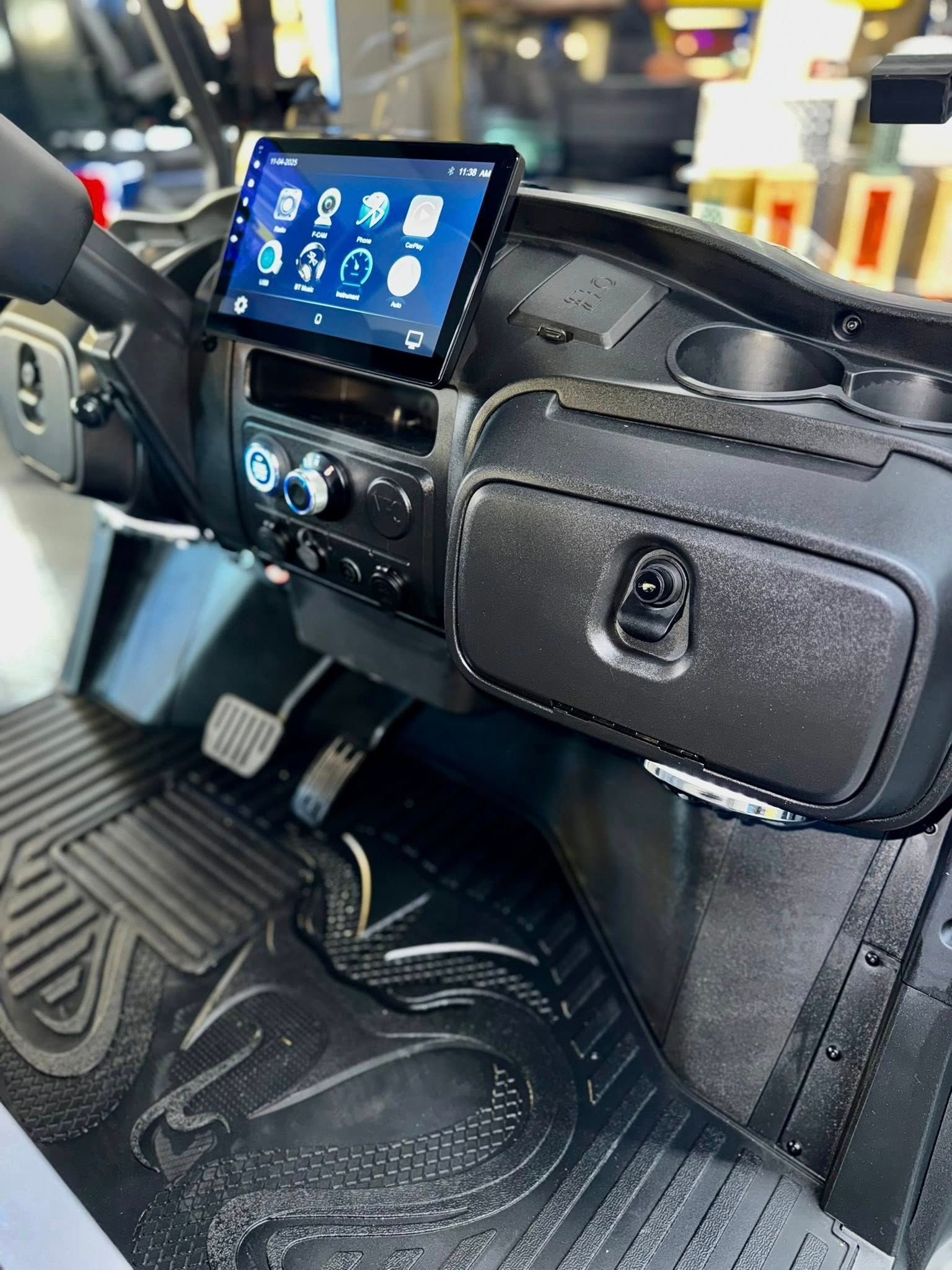 Black golf cart dashboard with touch screen, storage bag, cup holders, and floor mat.