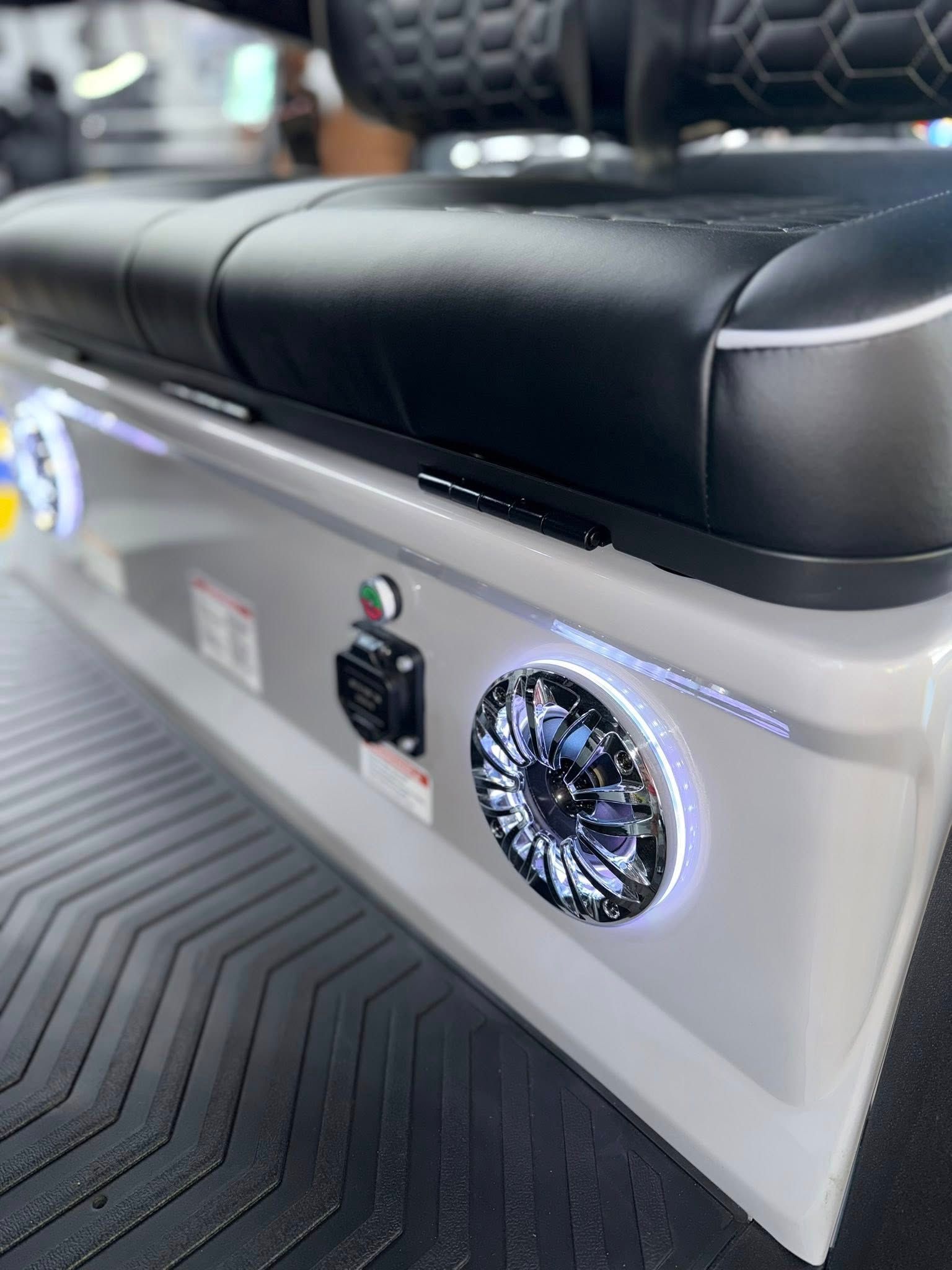 Close-up of a silver cart base with black seat, speakers, power outlet, and illuminated accents.