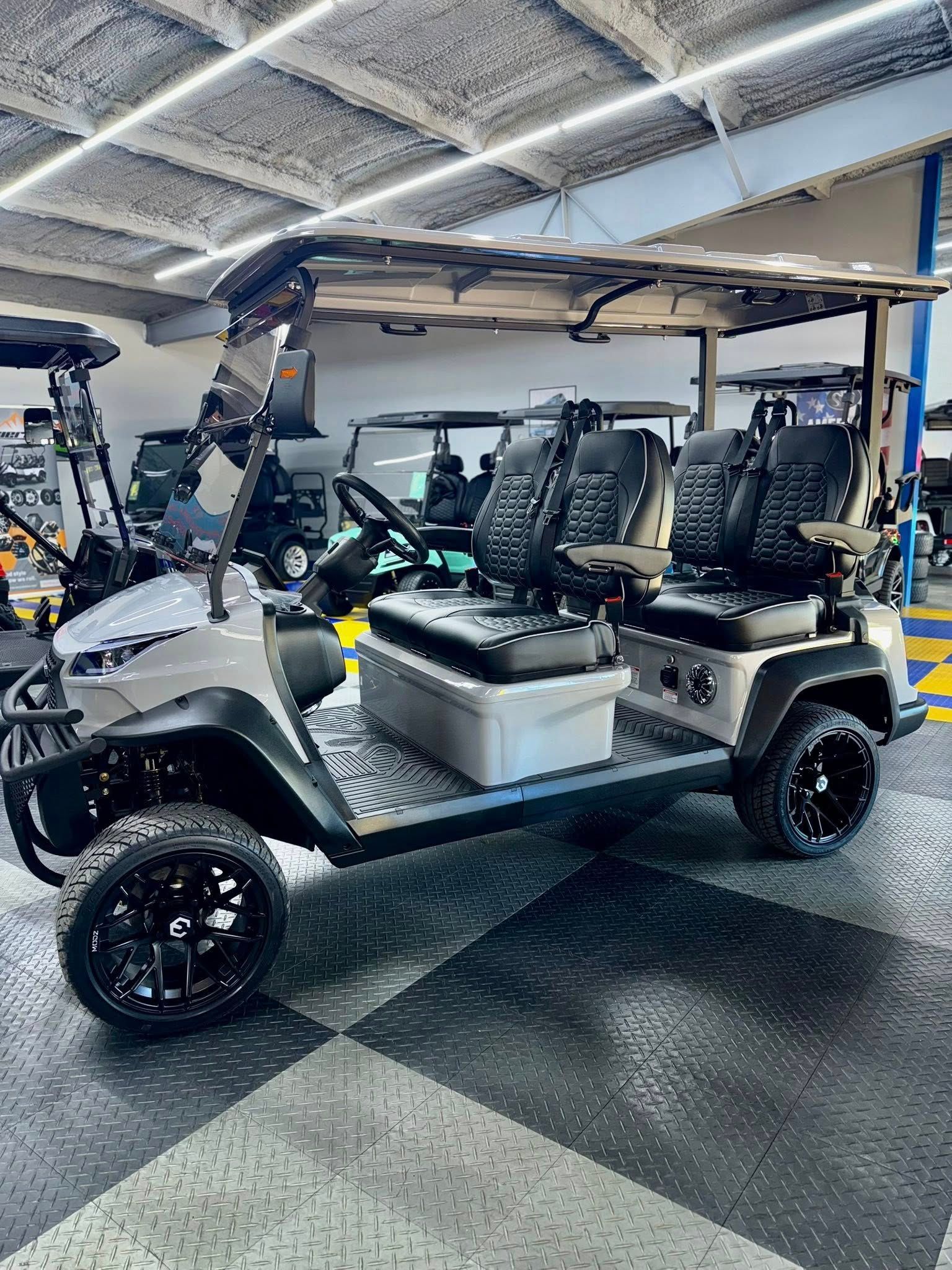 Gray golf cart with black wheels and seats, parked indoors.