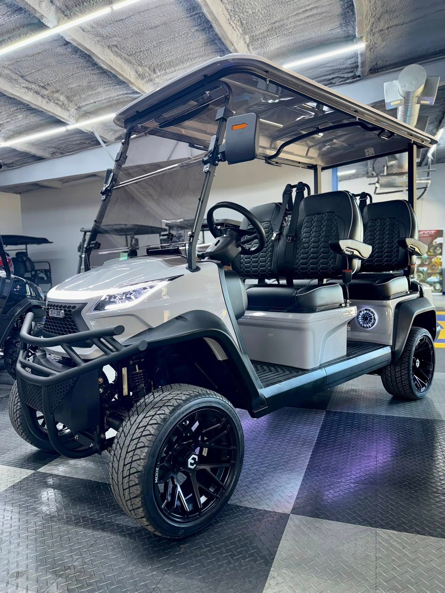 Gray golf cart with black accents, large wheels, and canopy indoors under bright lights.