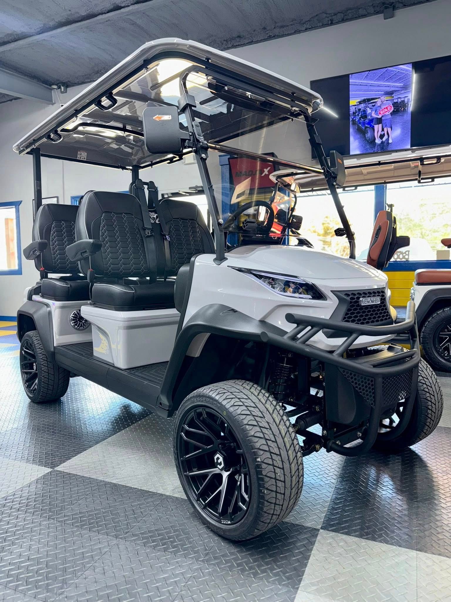 Gray and black custom golf cart on a checkered floor, black wheels, four seats, black canopy.