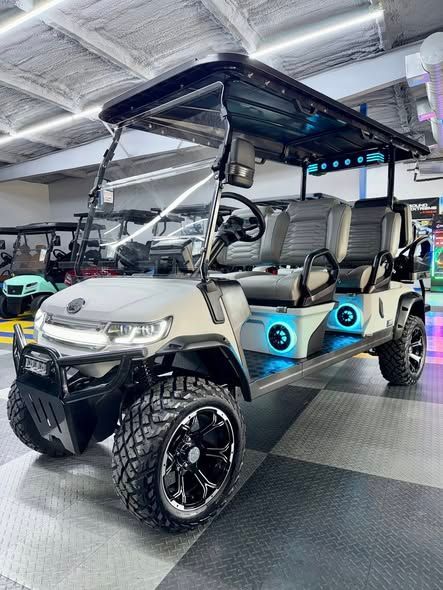 Customized six-seat golf cart with large tires, blue underglow lights, black accents, and a front bumper.