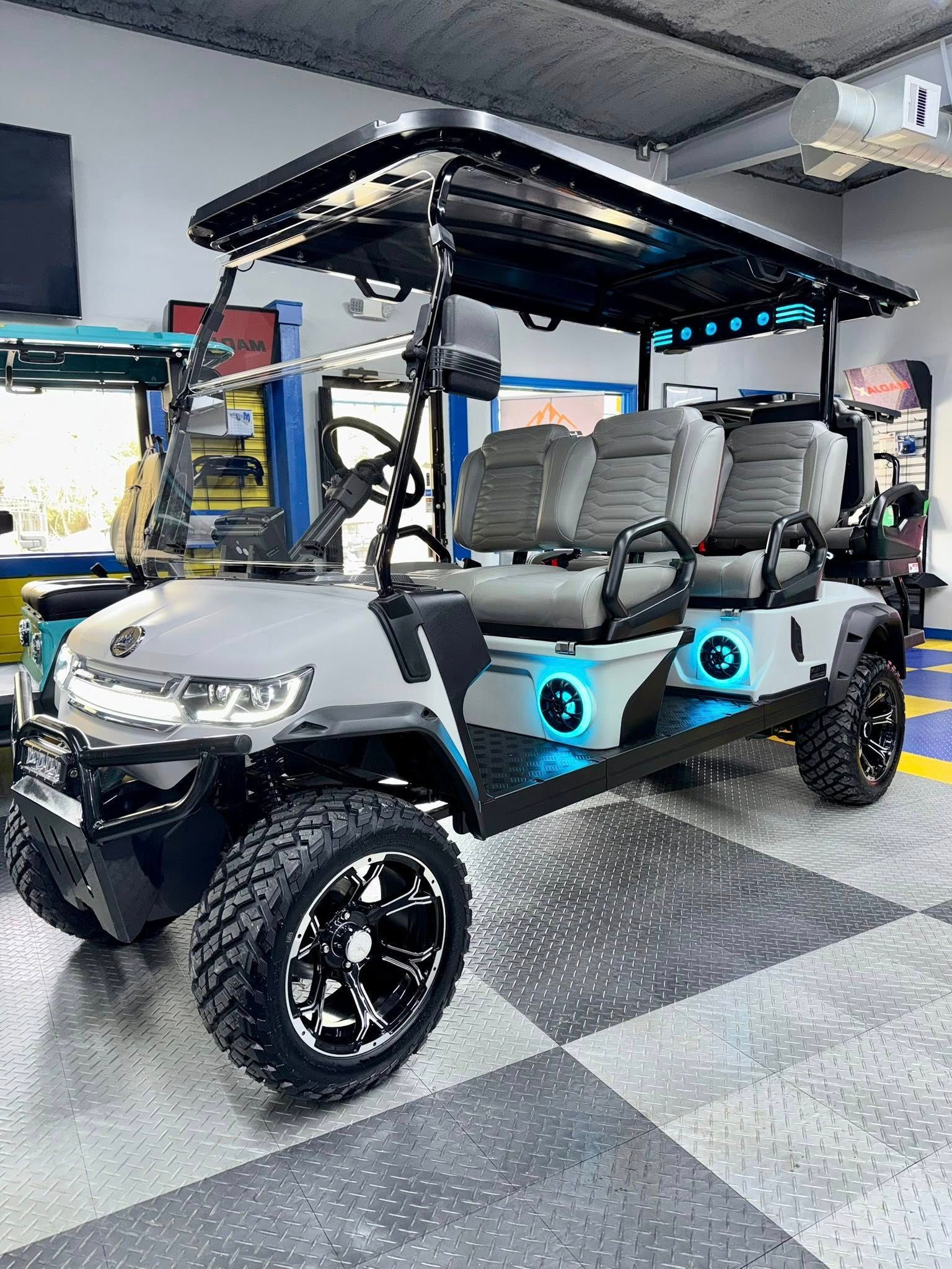 Gray custom golf cart with black wheels, LED lights, and seating for six, indoors.