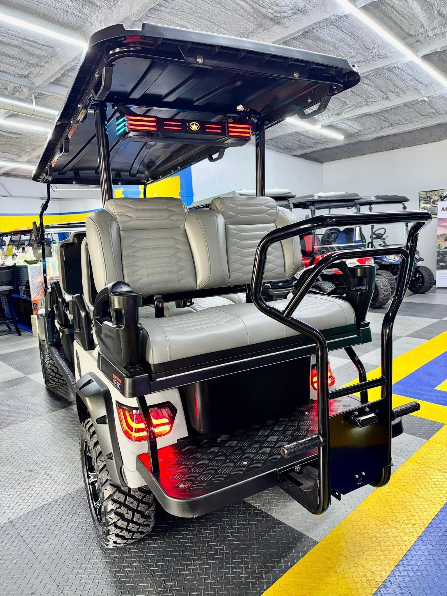 White and black golf cart with off-road tires, a black roof, and gray seats, indoors.