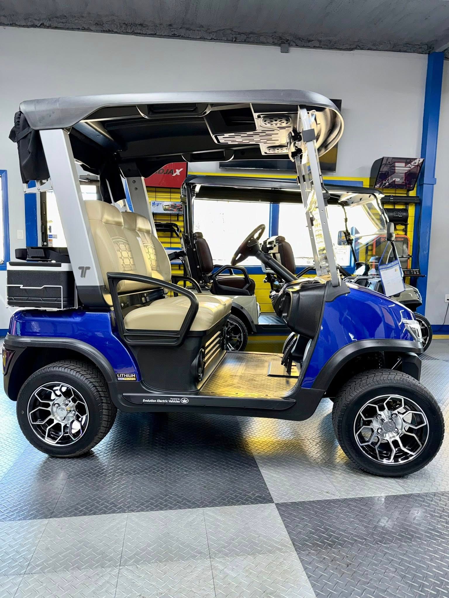 Blue and black golf cart with tan seats and black roof, parked inside a showroom.