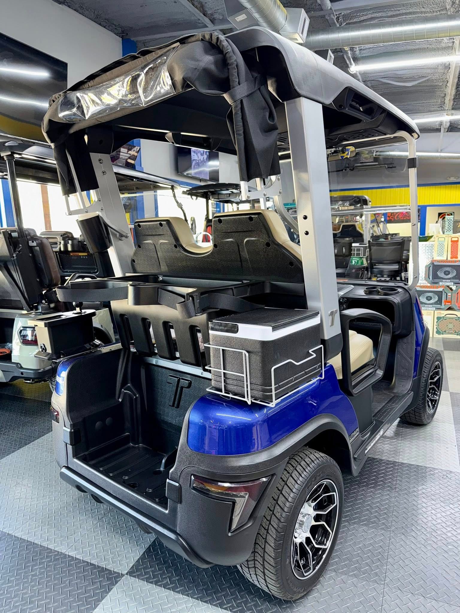 Blue golf cart with black accents, black and tan seats, and a cooler.