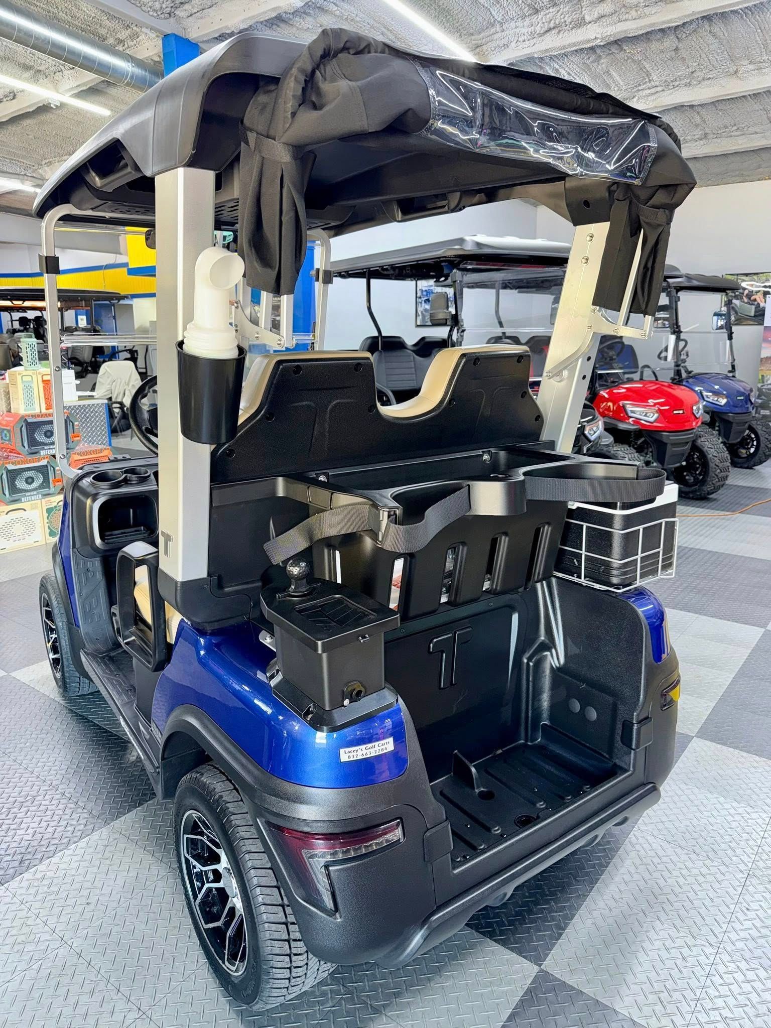 Blue golf cart with black accessories, parked indoors.